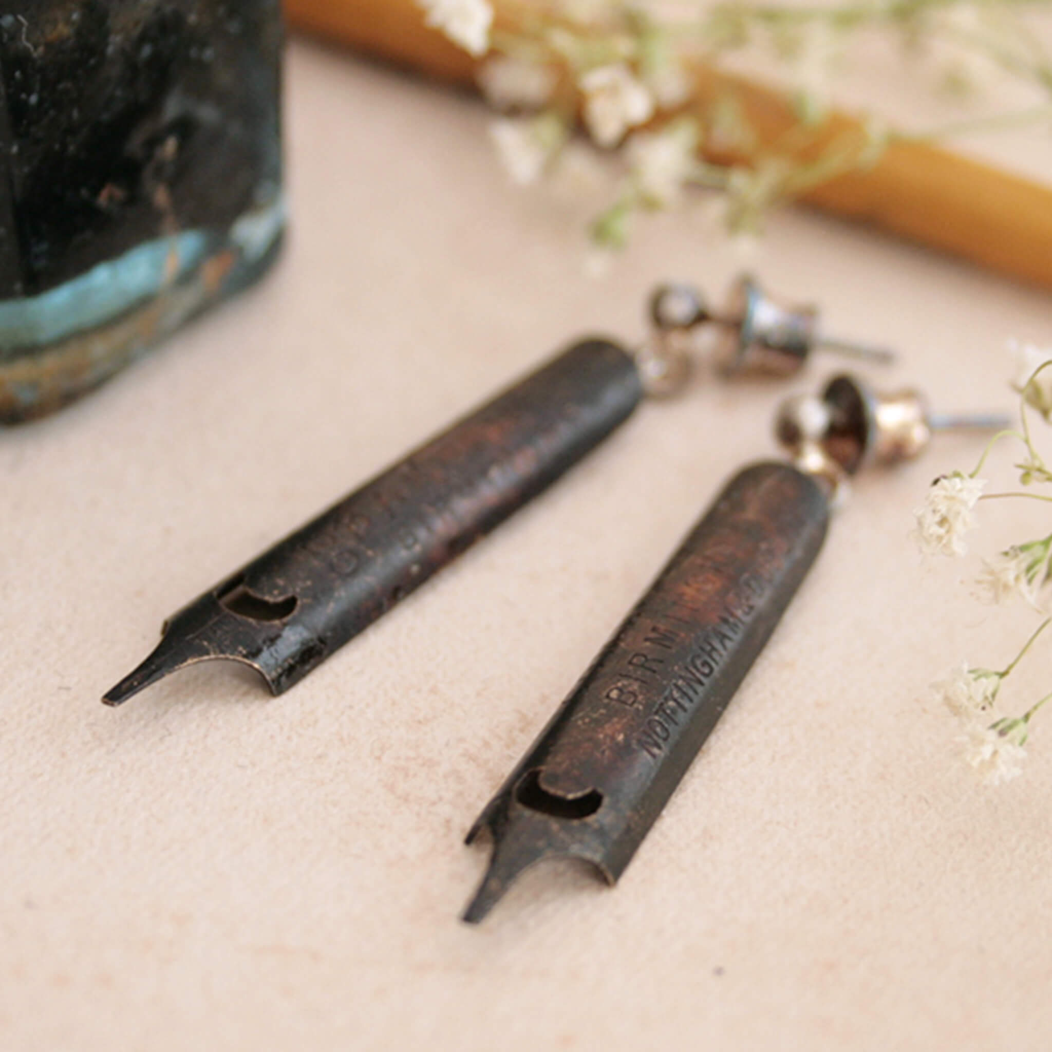 antique gold pen nib earrings covered in heavy patina lying on a coloured card