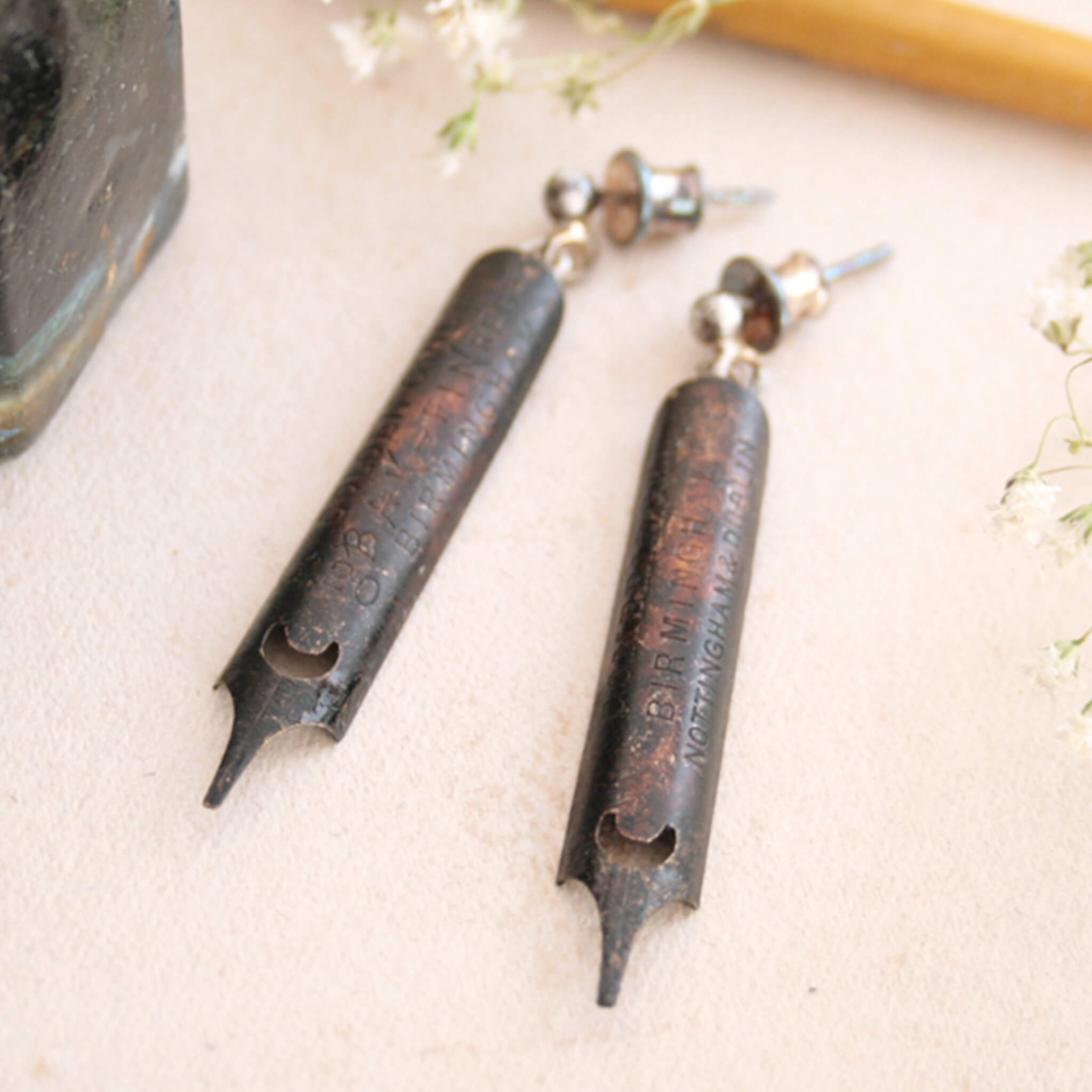 antique gold pen nib earrings covered in heavy patina lying on a coloured card