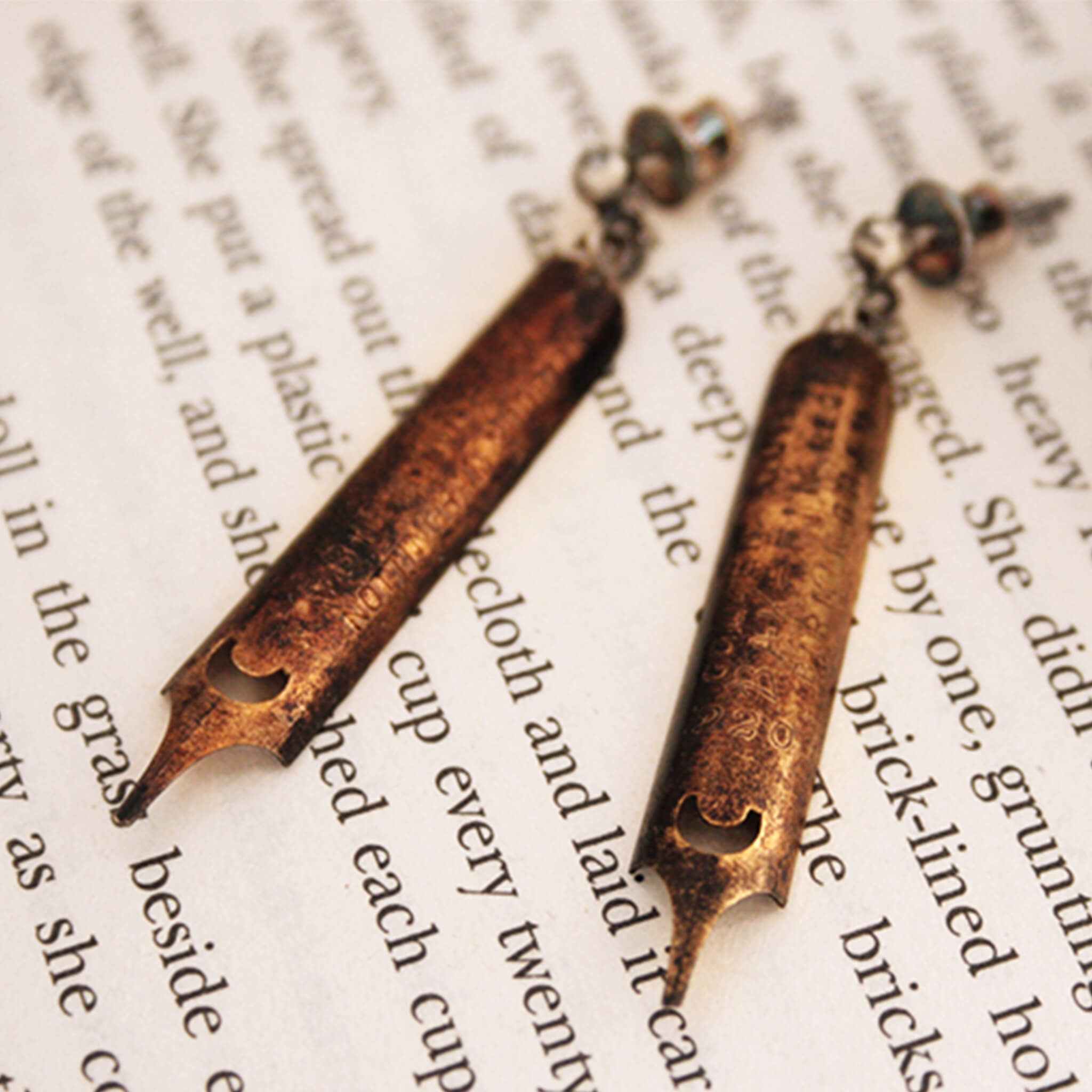 antique gold pen nib earrings covered in patina lying on a page of text