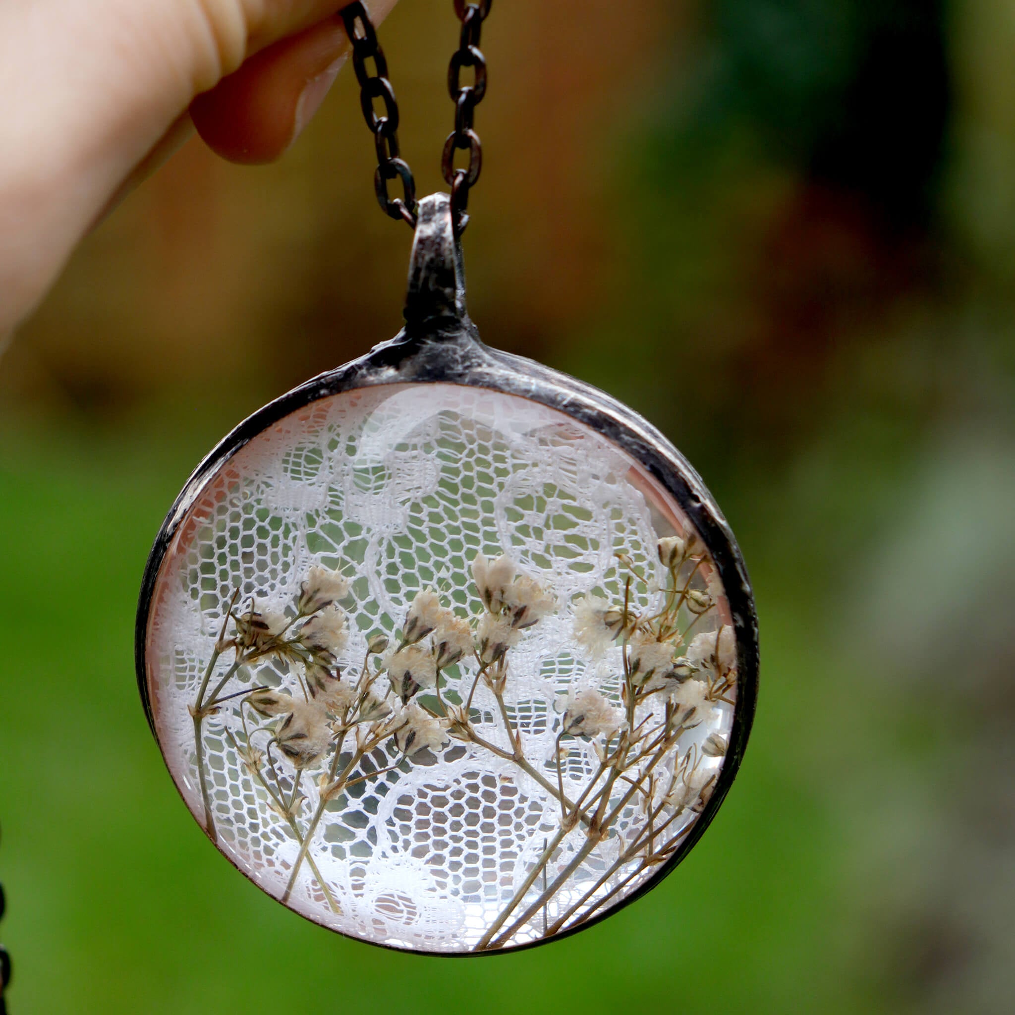 Pressed flowers in a stained glass necklace hold in hand hanging on a green background