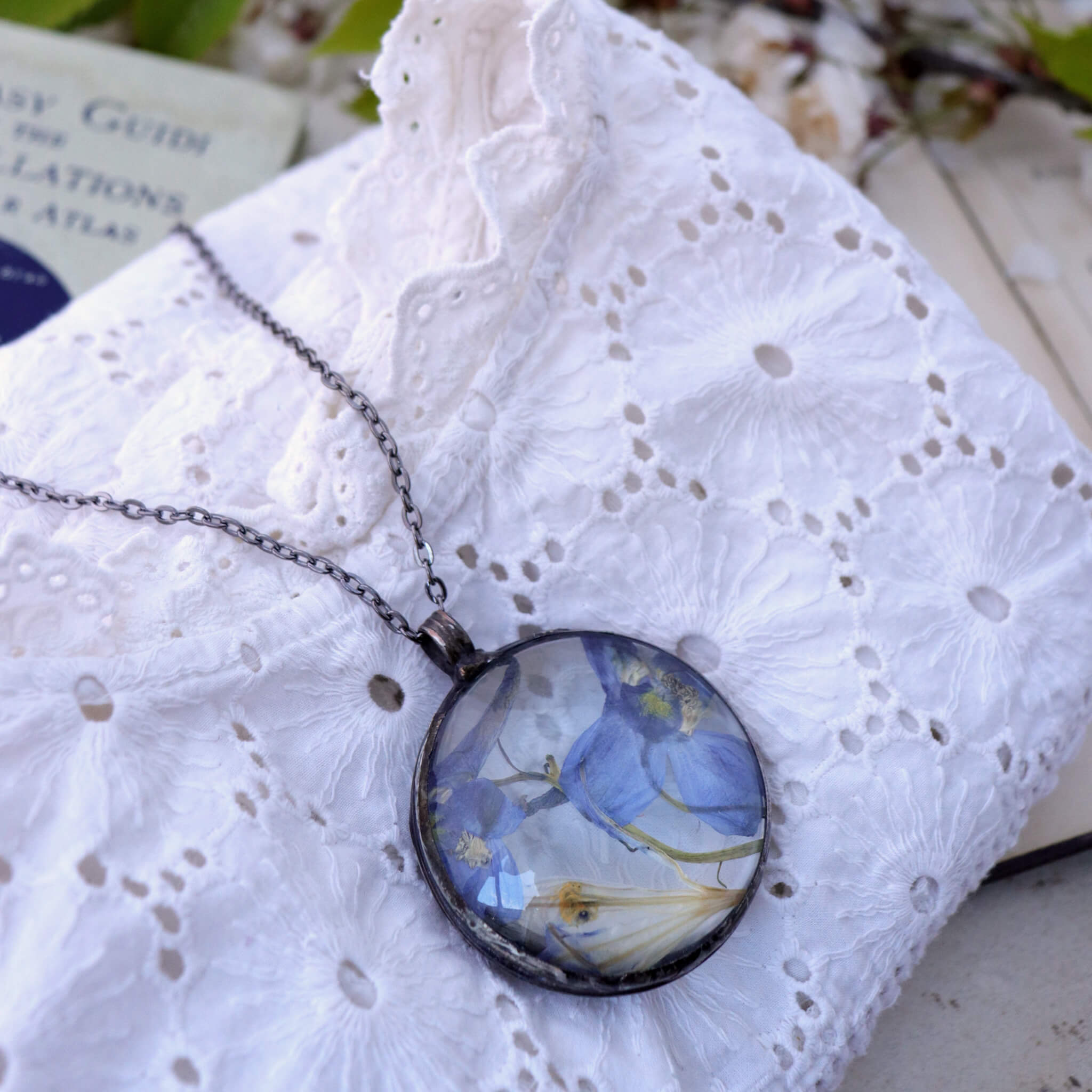 Blue pressed flower in a large round glass soldered necklace lying on a white blouse