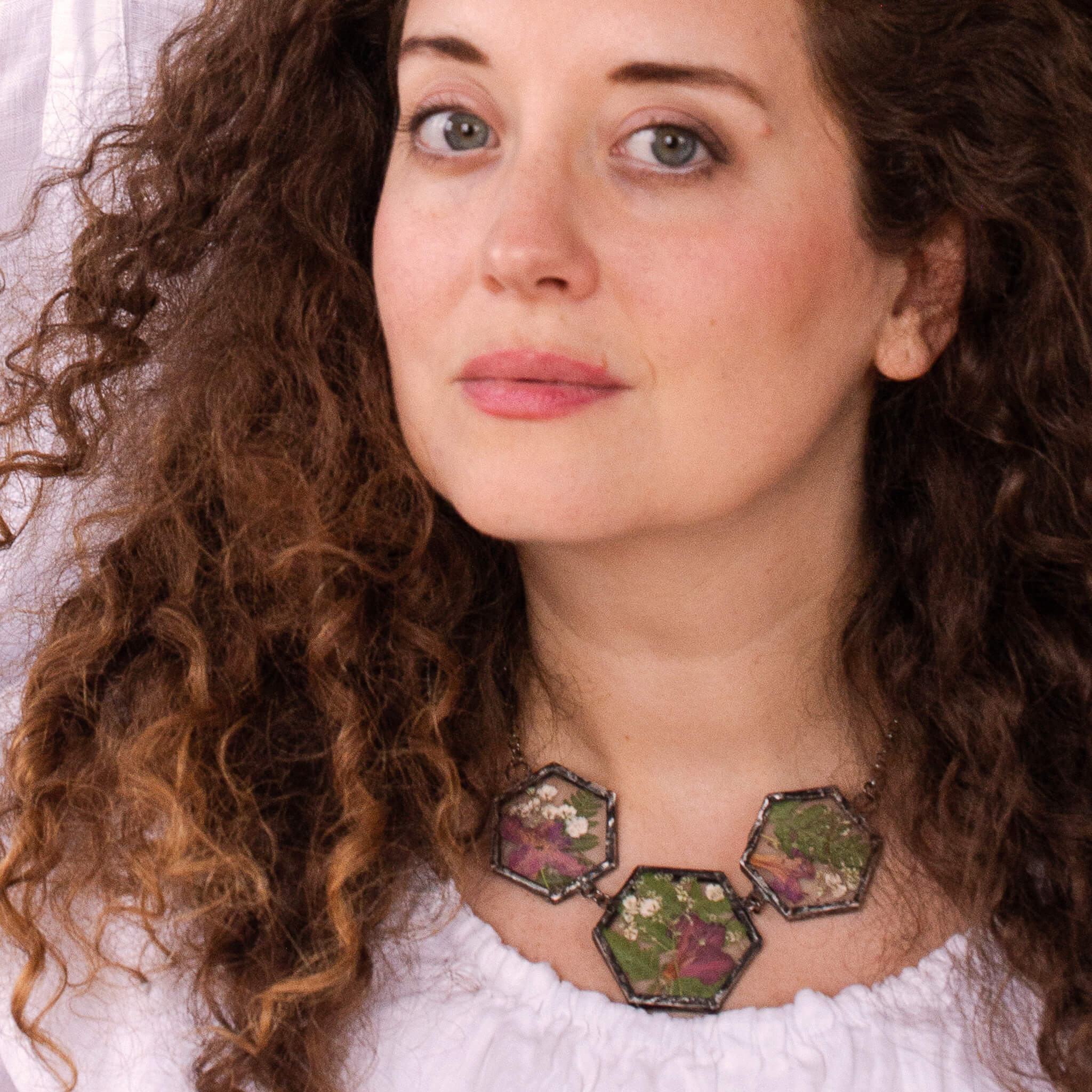 Curly haired brunette in white blouse wearing a statement necklace