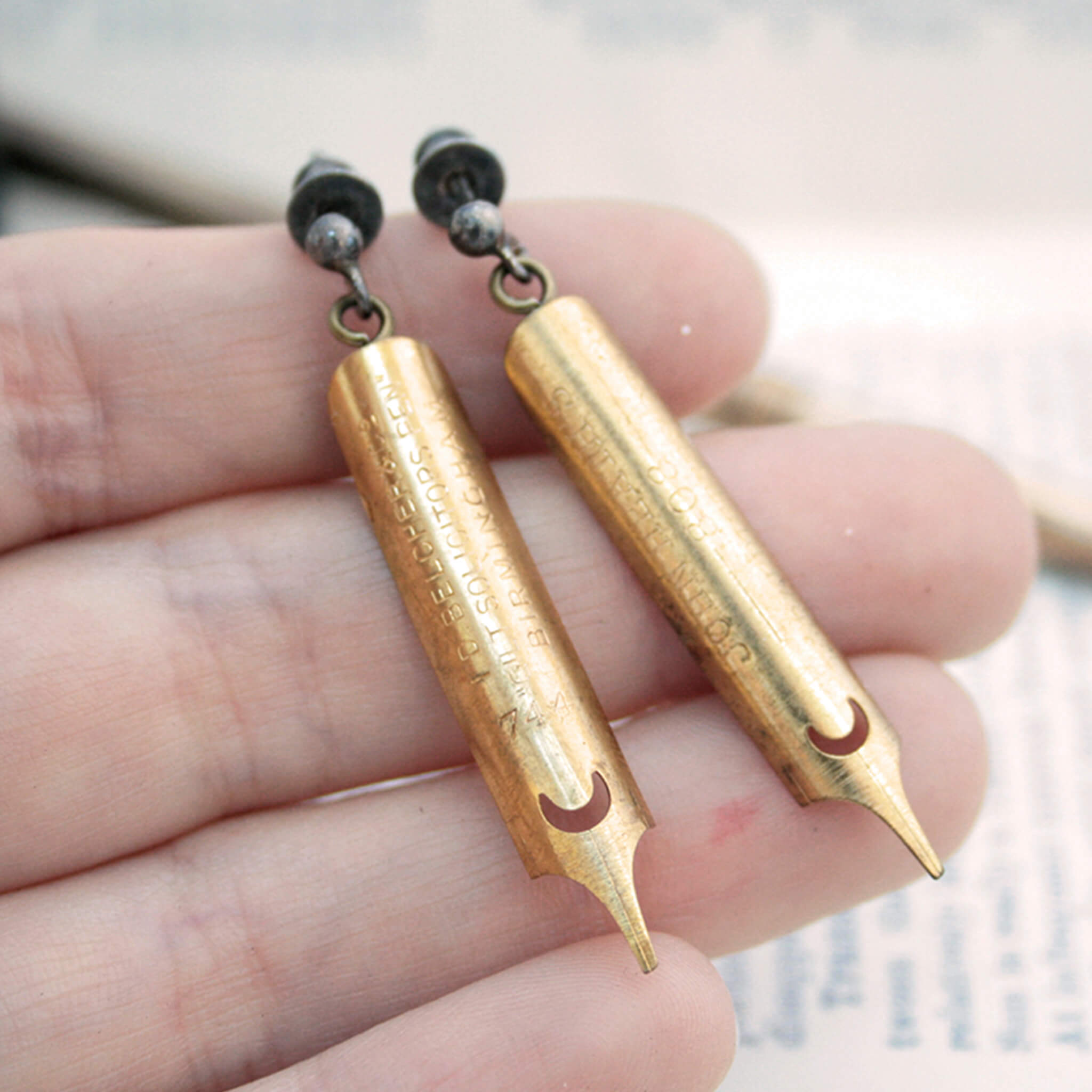 gold coated pen nib earrings lying on a hand
