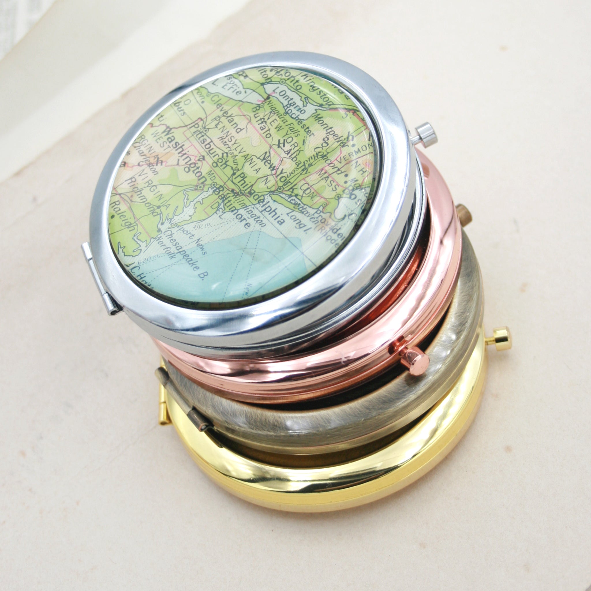 Four compact mirrors one on the another, gold, bronze,rose gold and silver featuring map of New York