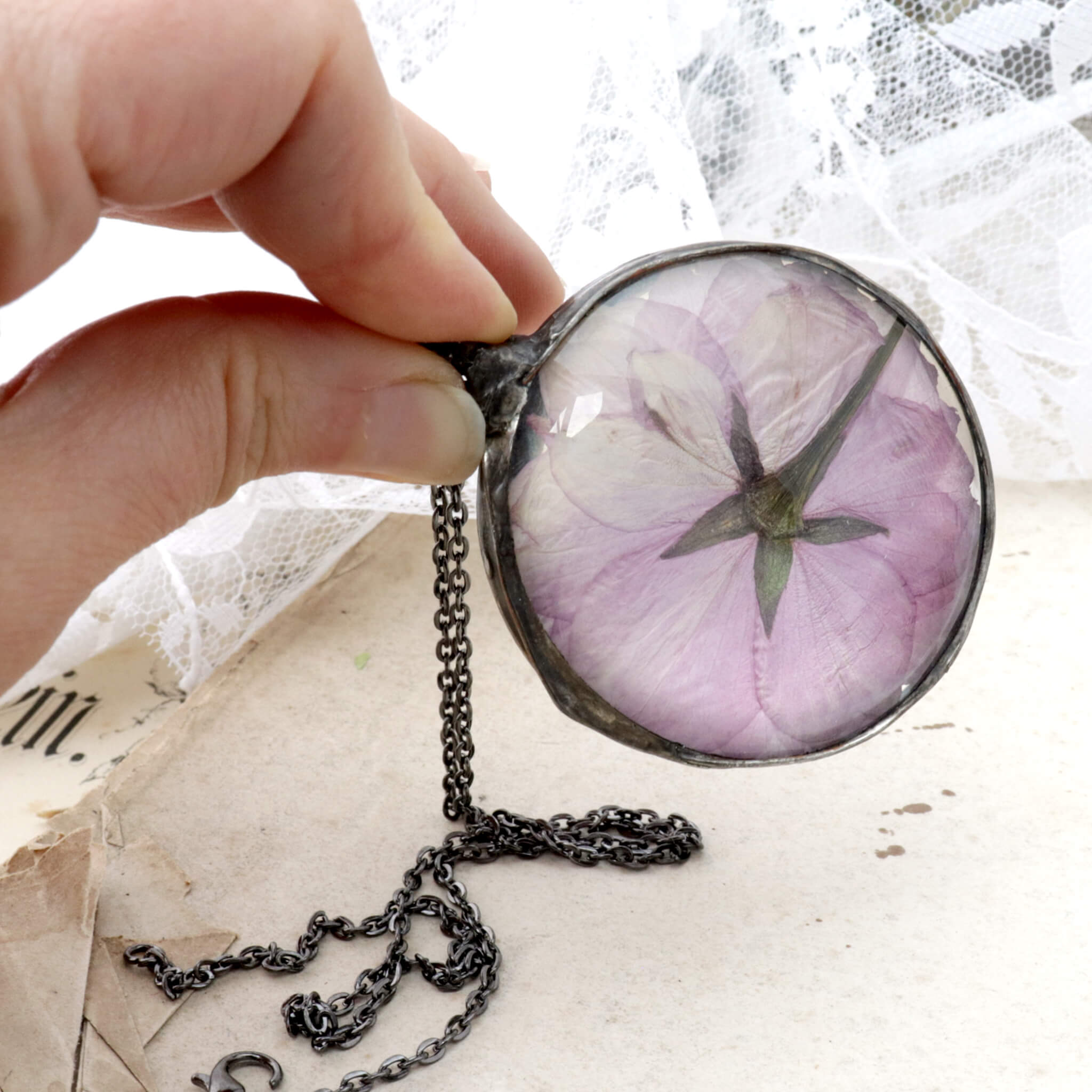 Round cherry blossom necklace being hold between thumb and index finger