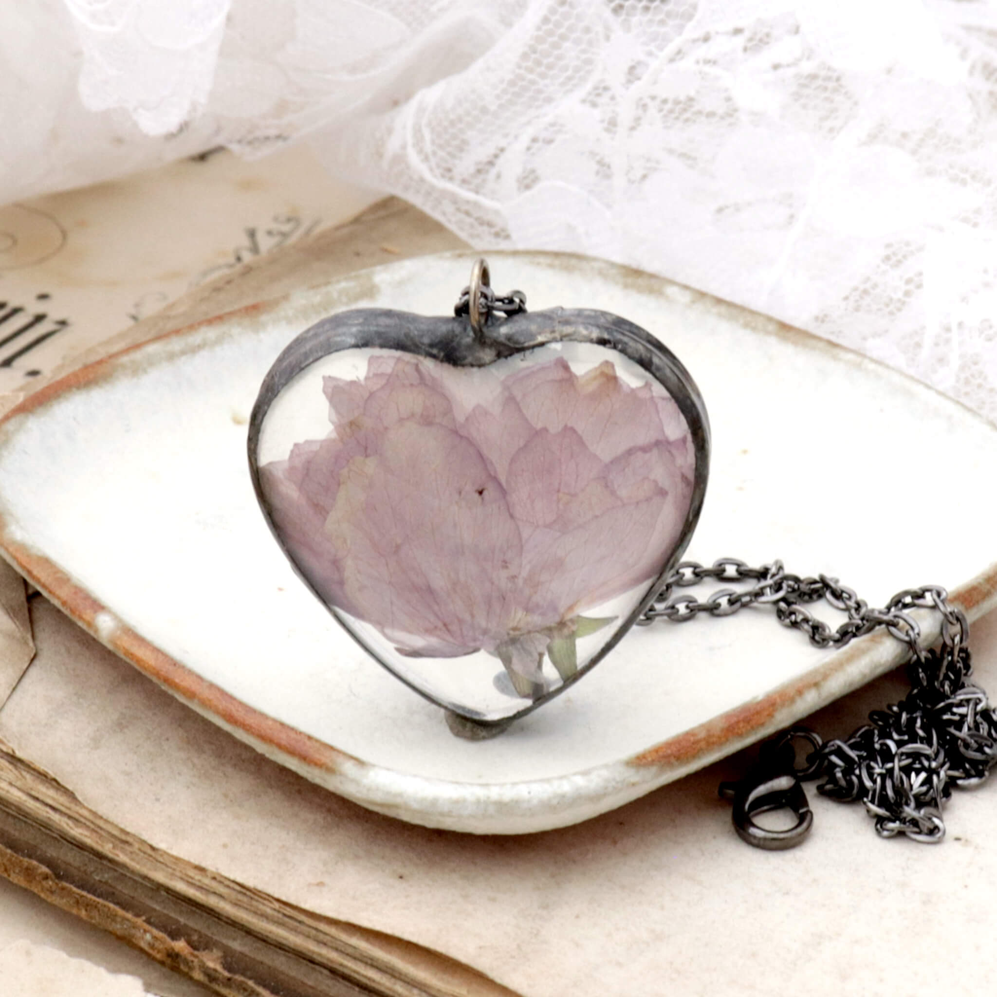 Heart shaped cherry blossom necklace standing on the edge on a little white dish