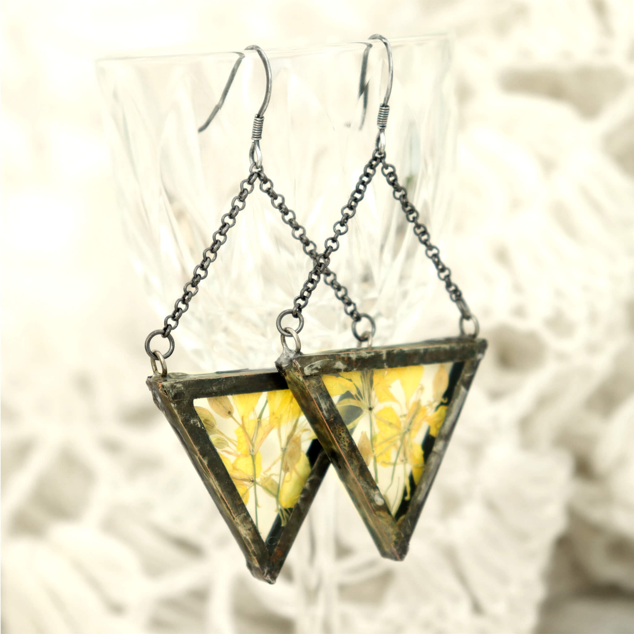 Triangular pressed yellow flower earrings hanging from an edge of a glass