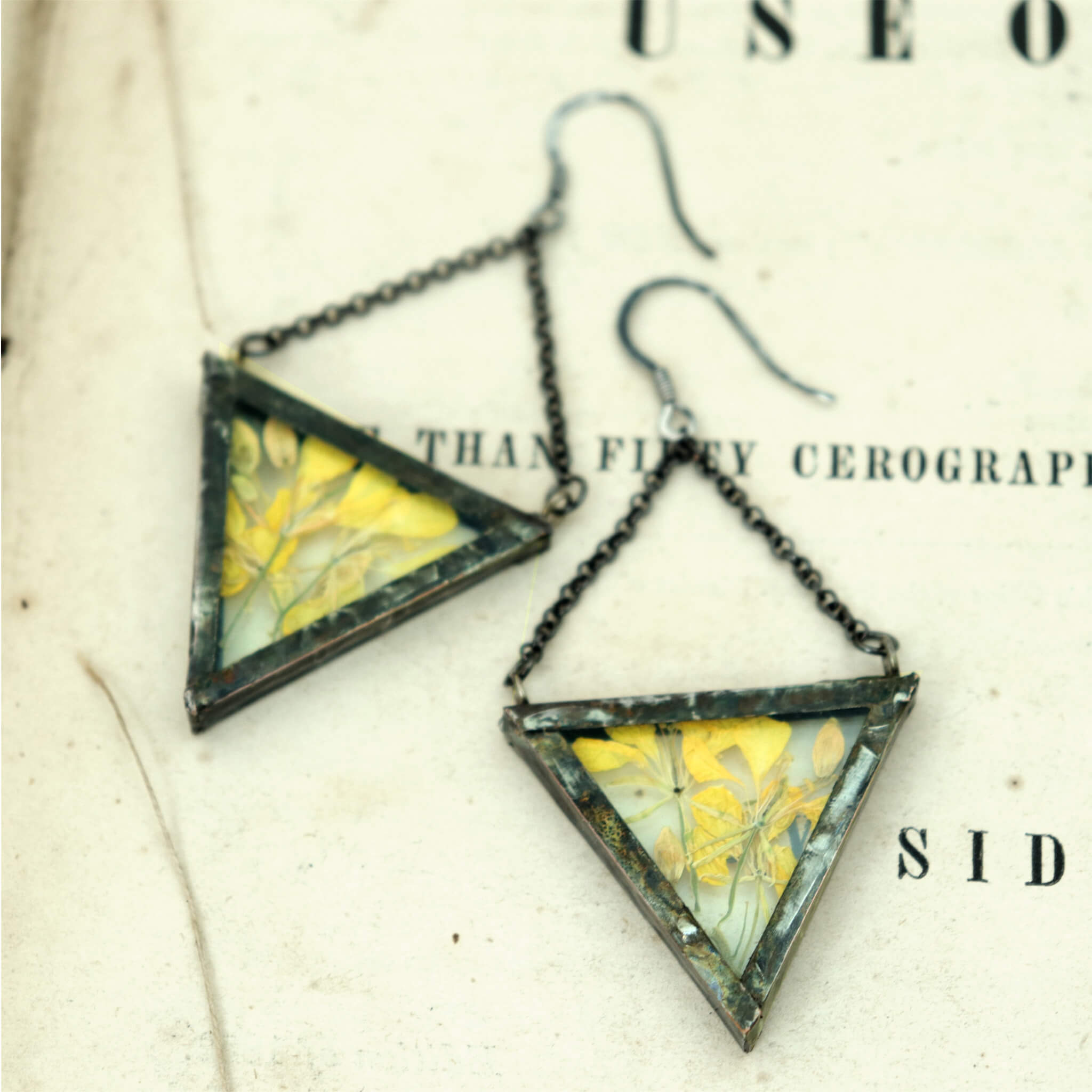Triangular pressed yellow flowers earrings lying on an old book