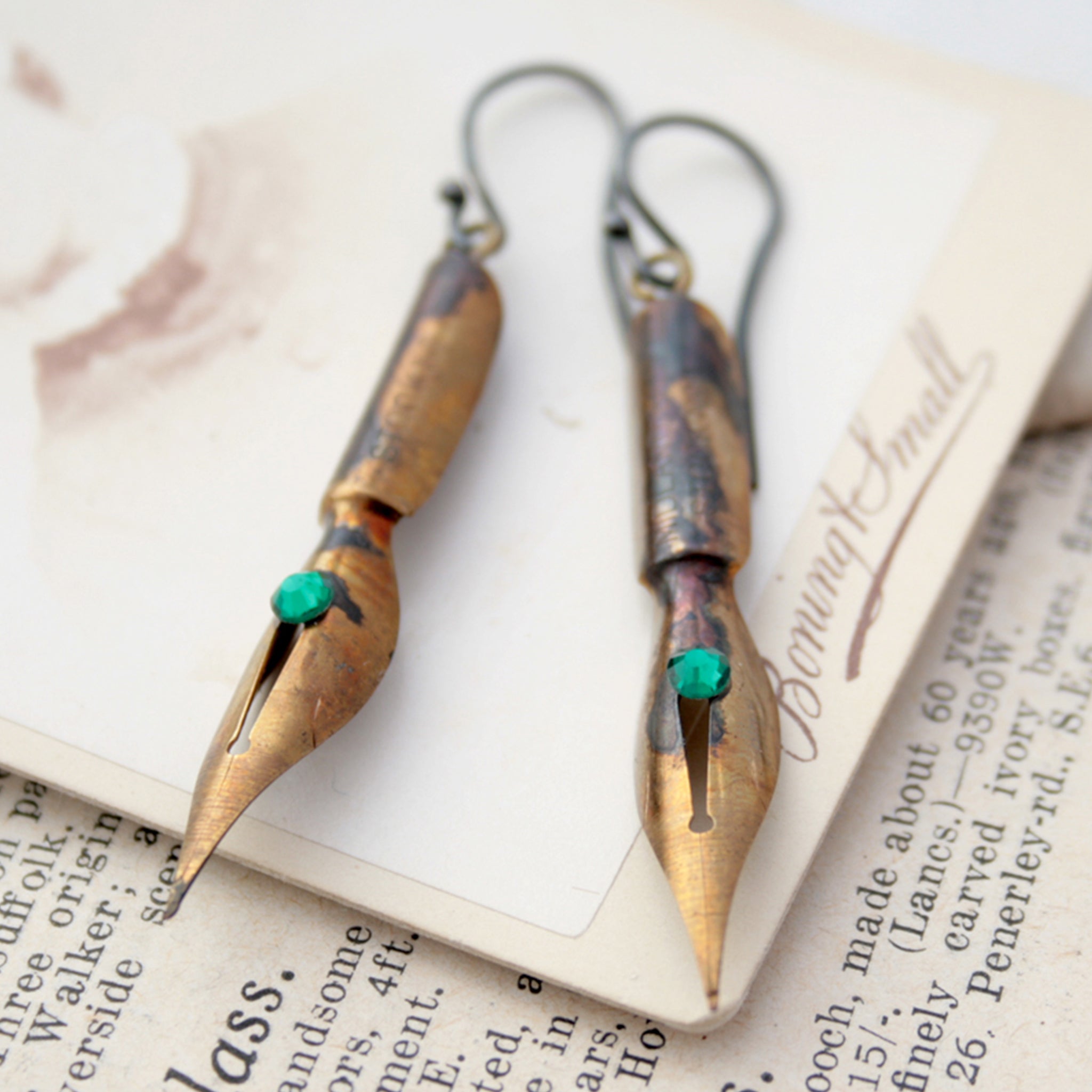 gold earrings made of real pen nibs with turquoise crystals lying on an old photograph