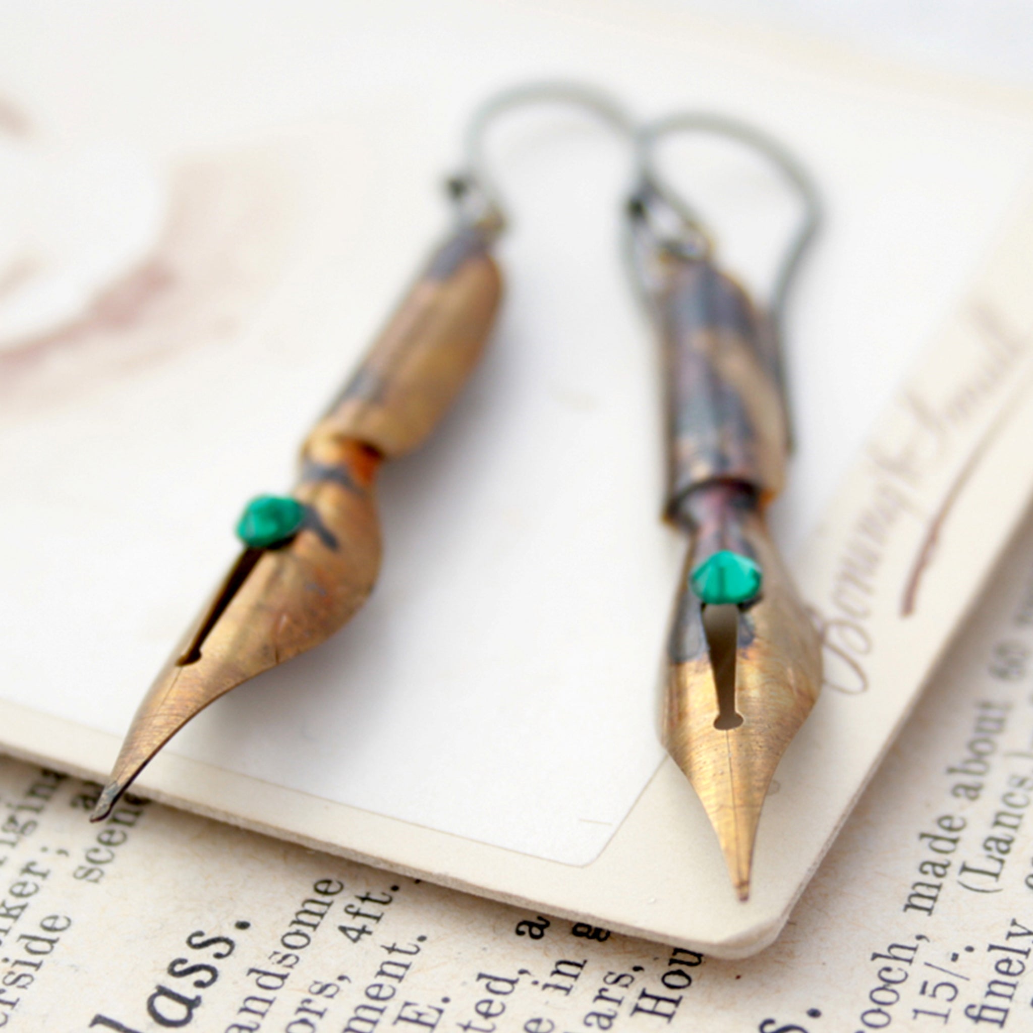gold earrings made of real pen nibs with turquoise crystals lying on an old photograph
