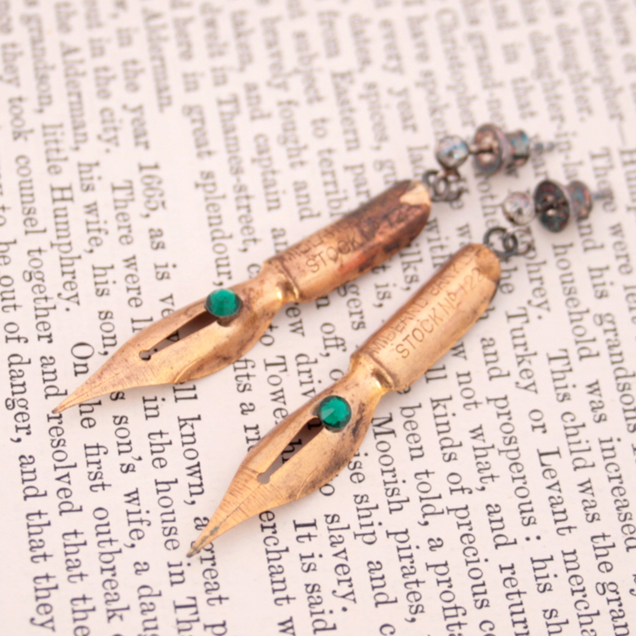gold earrings made of real pen nibs with turquoise crystals lying on an old newspaper