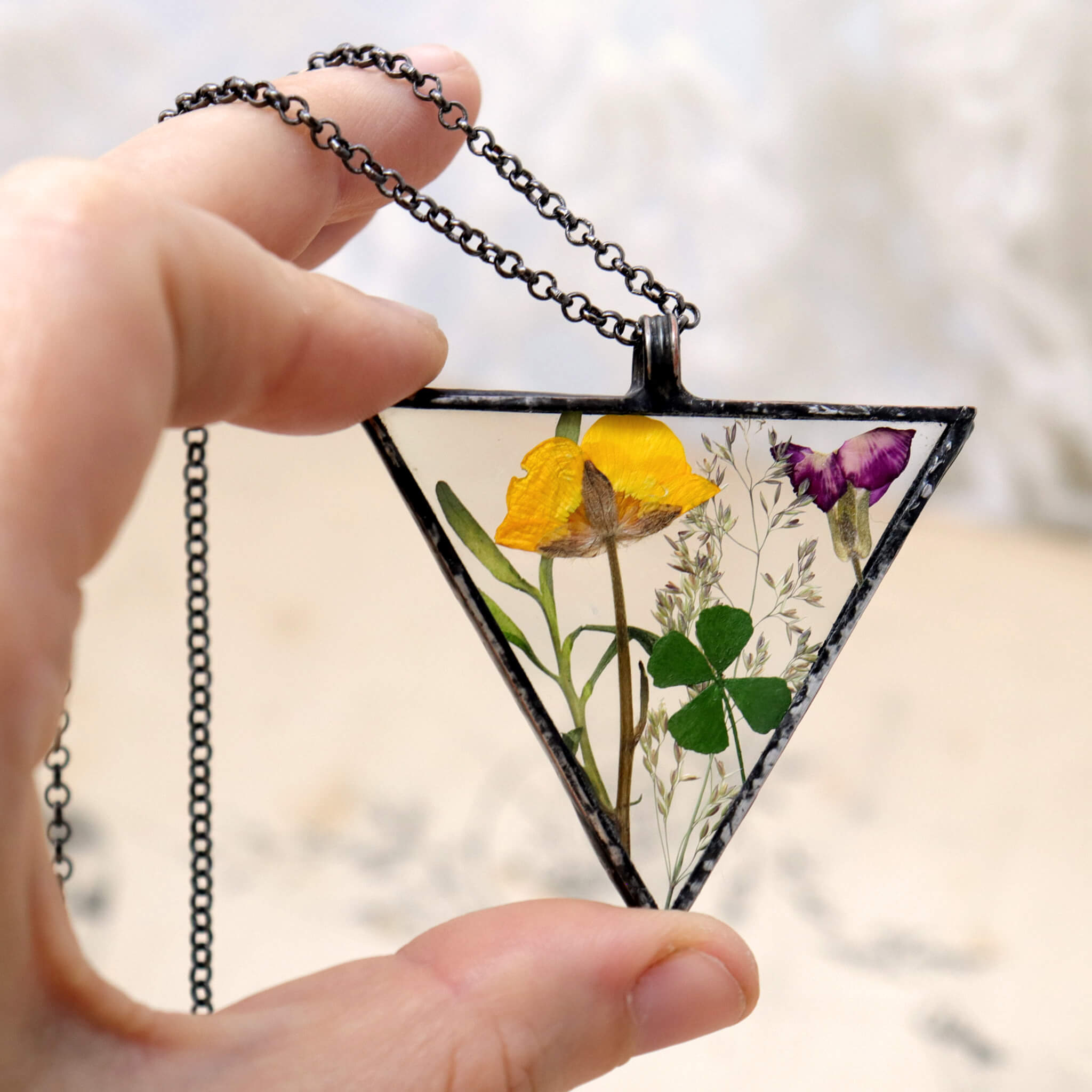 Hand holding Triangular yellow and green pressed flowers necklace