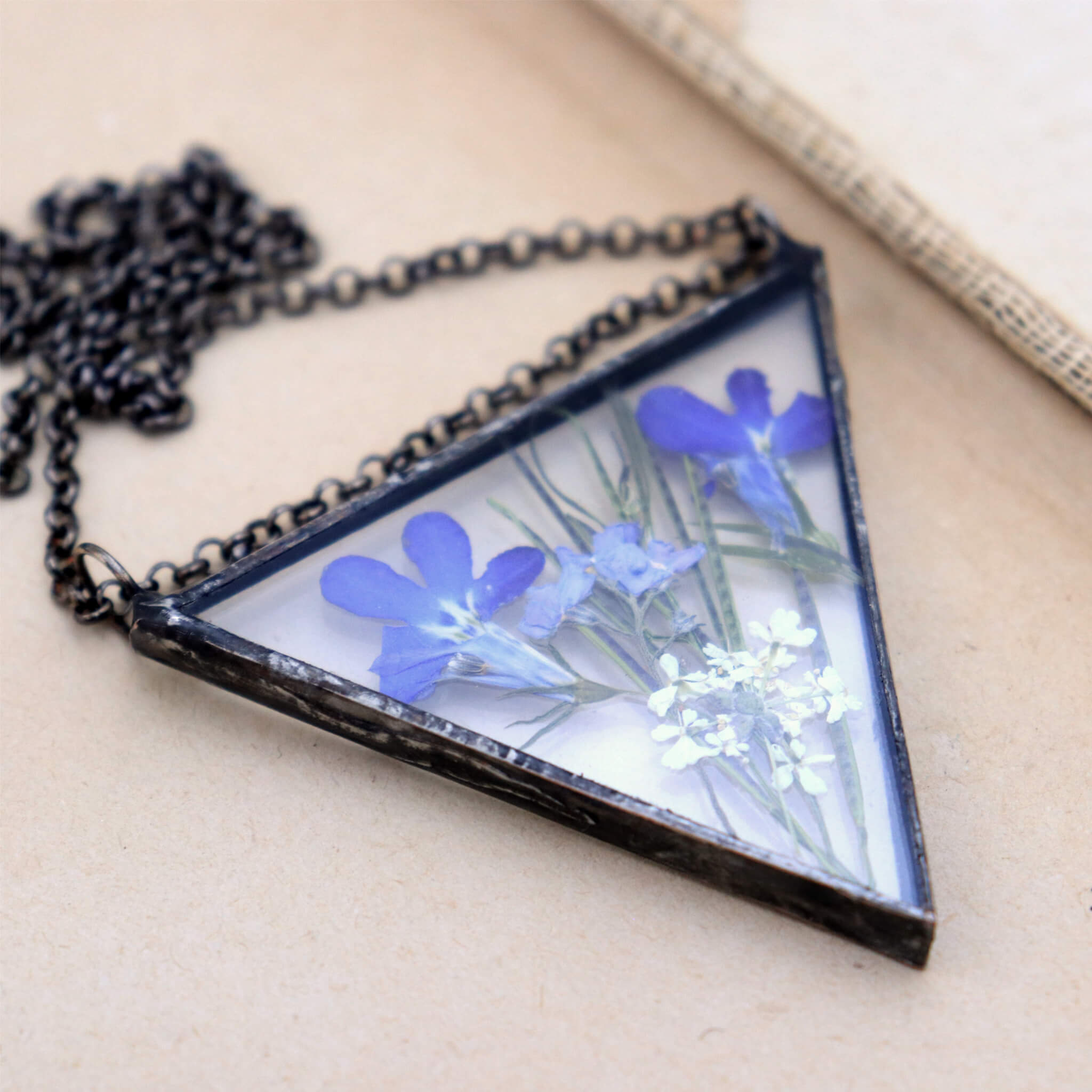 Triangular pressed lobelia flowers necklace lying on a vintage book