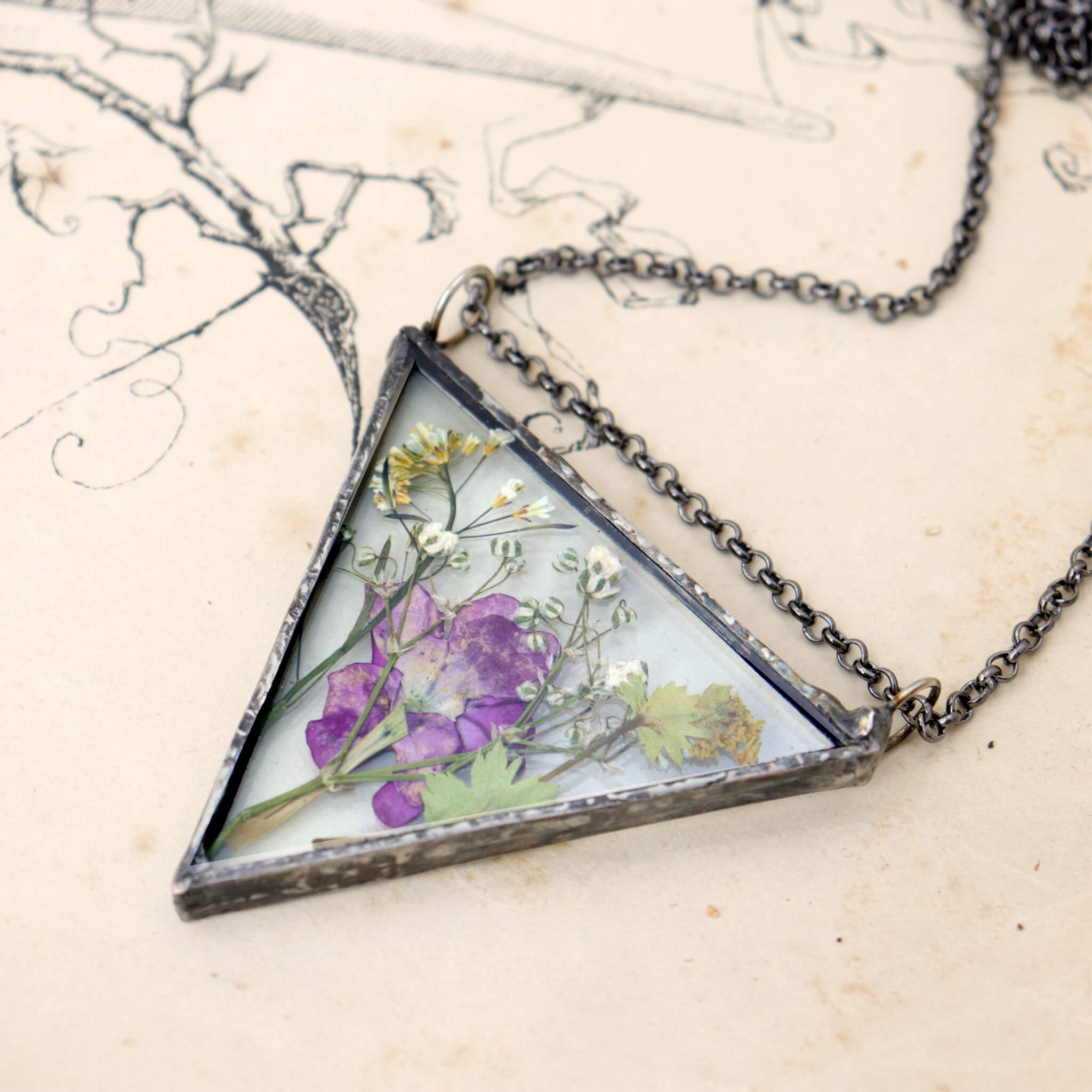 Triangular pressed pink flower necklace lying on an old book