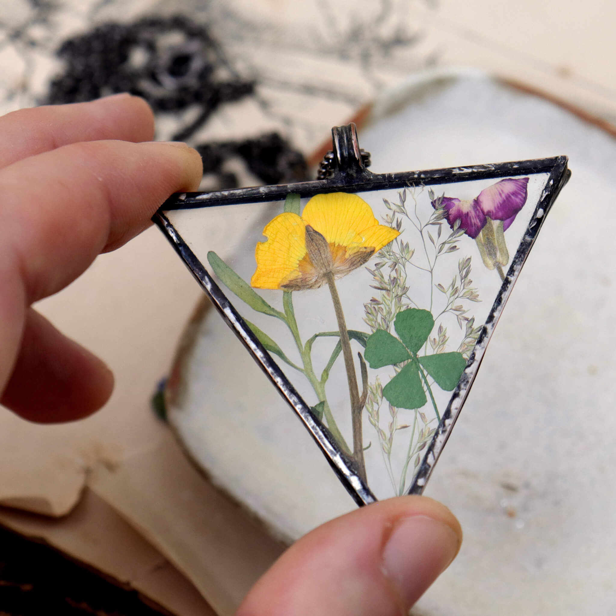 Hand holding Triangular yellow and green pressed flowers necklace