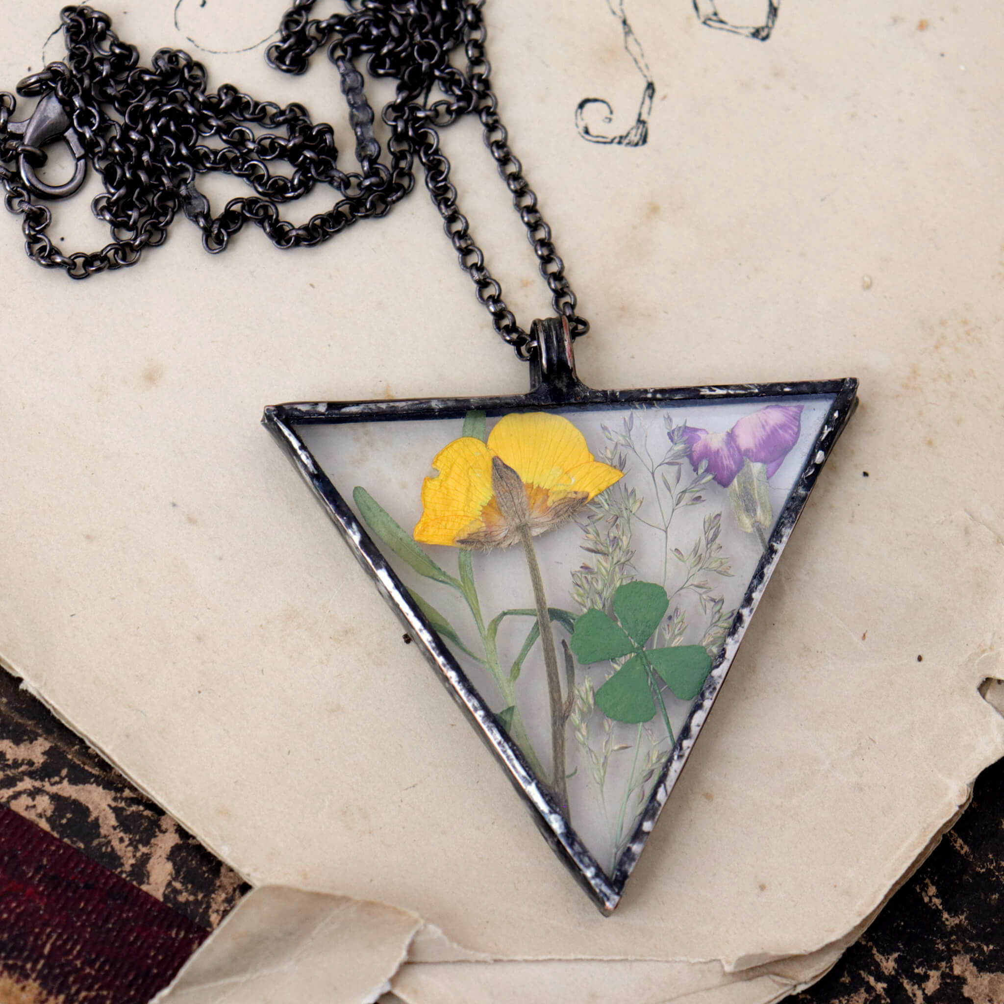 Triangular yellow and green pressed flowers necklace lying on a vintage book