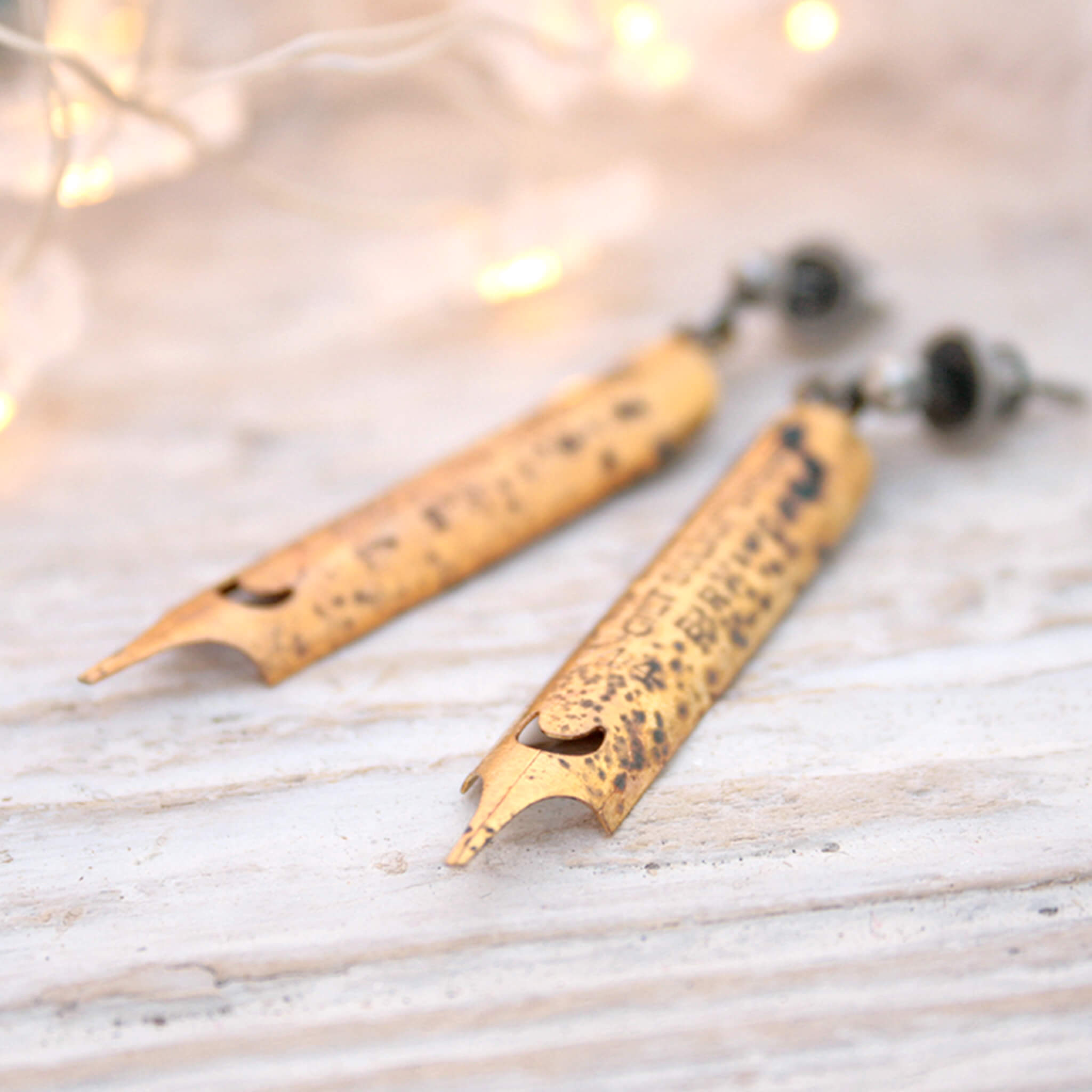 gold coated pen nib earrings with some patina markings lying on a white board