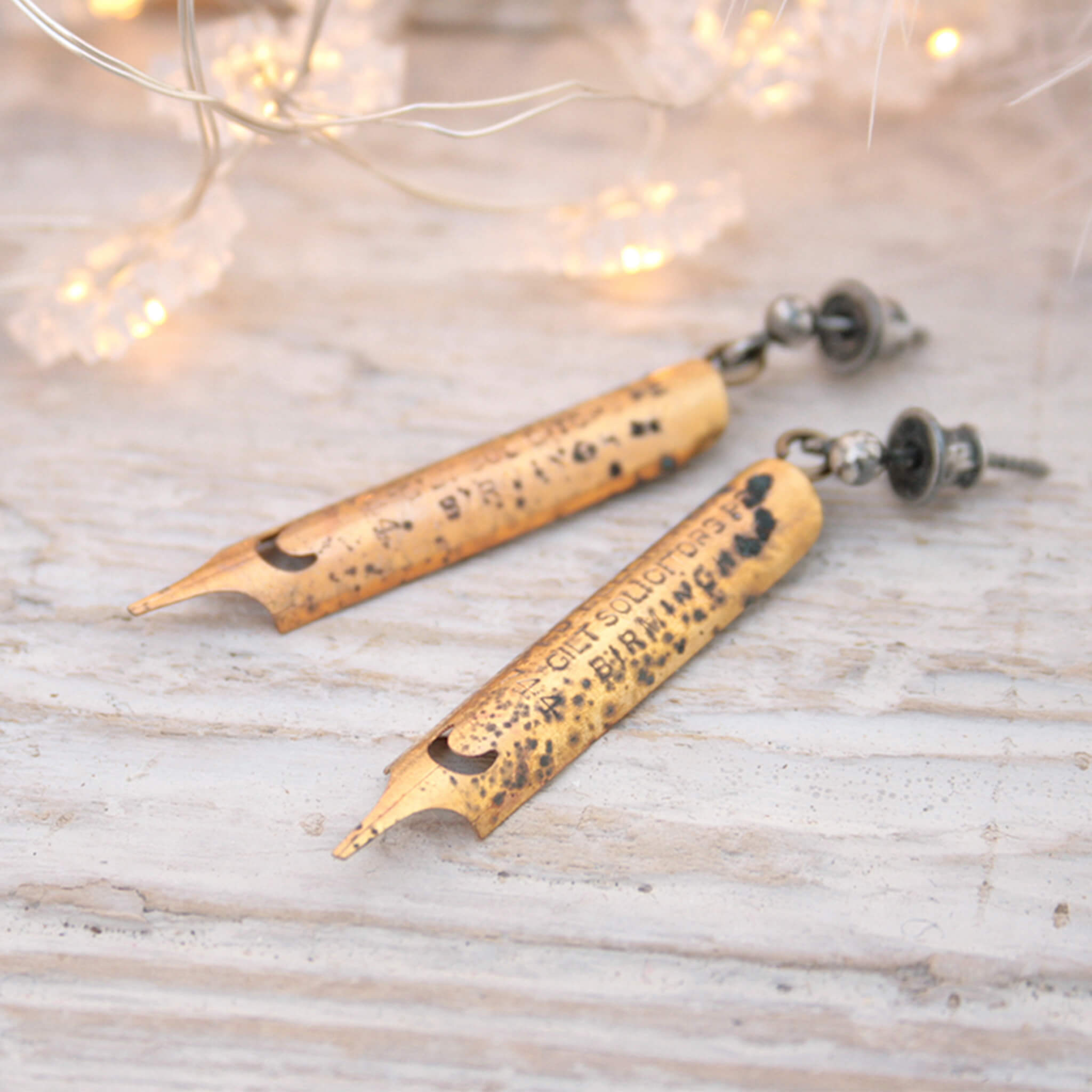 gold coated pen nib earrings with some patina markings lying on a white board