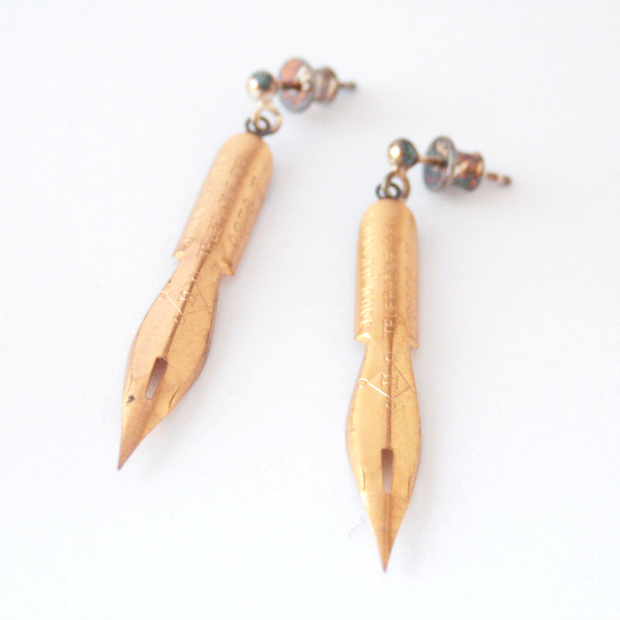 gold earrings made of real pen nibs lying on a white paper