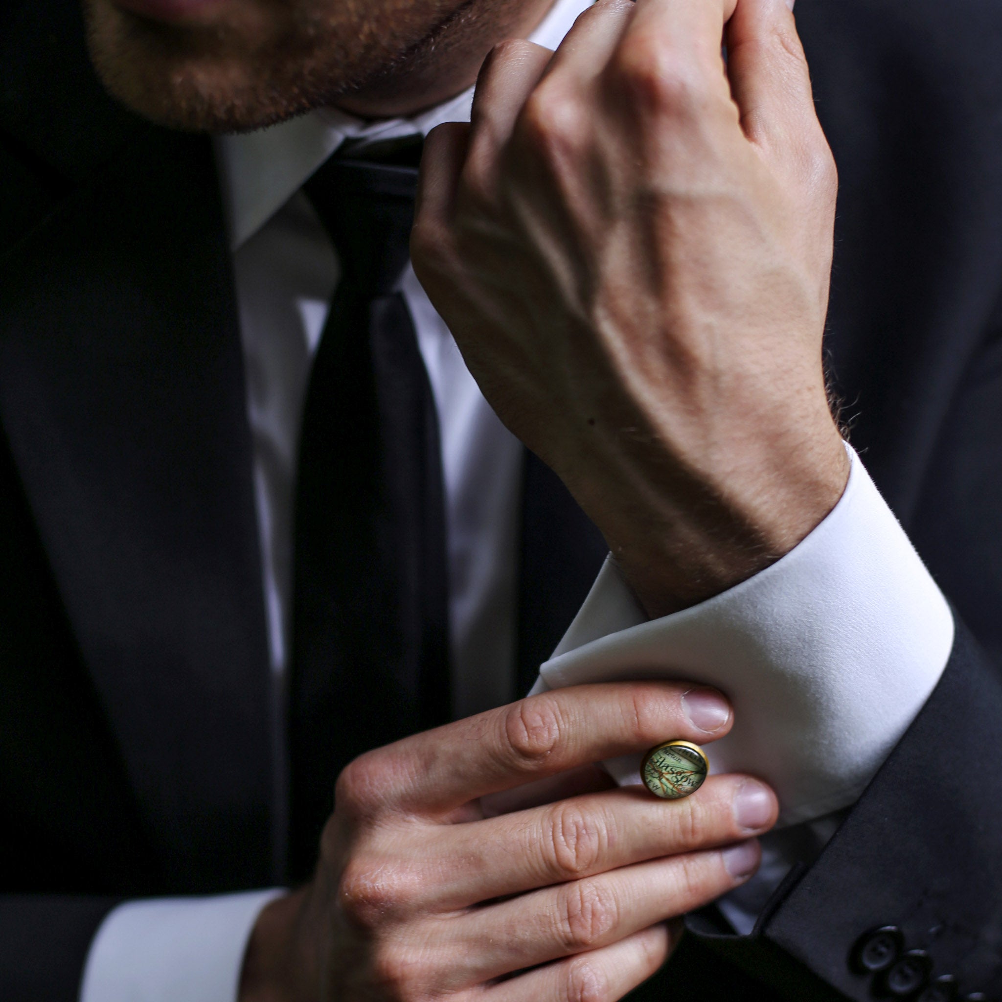 Man in a suit putting on pair of map cufflinks