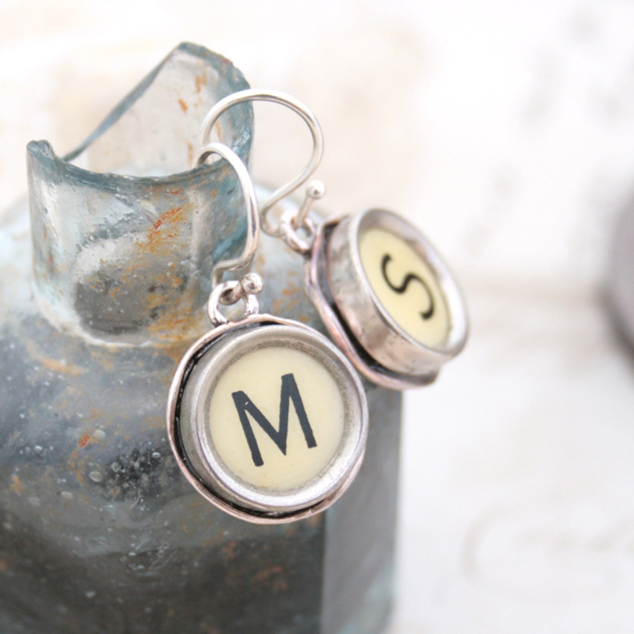 M and S Ivory Typewriter keys turned into initial earrings hanging on the edge of inkwell