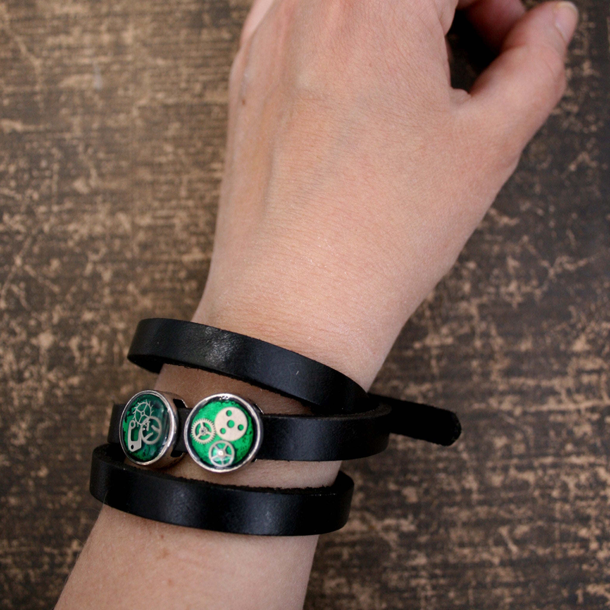 Black leather triple wrap bracelet with green steampunk slider beads with watch parts on hand
