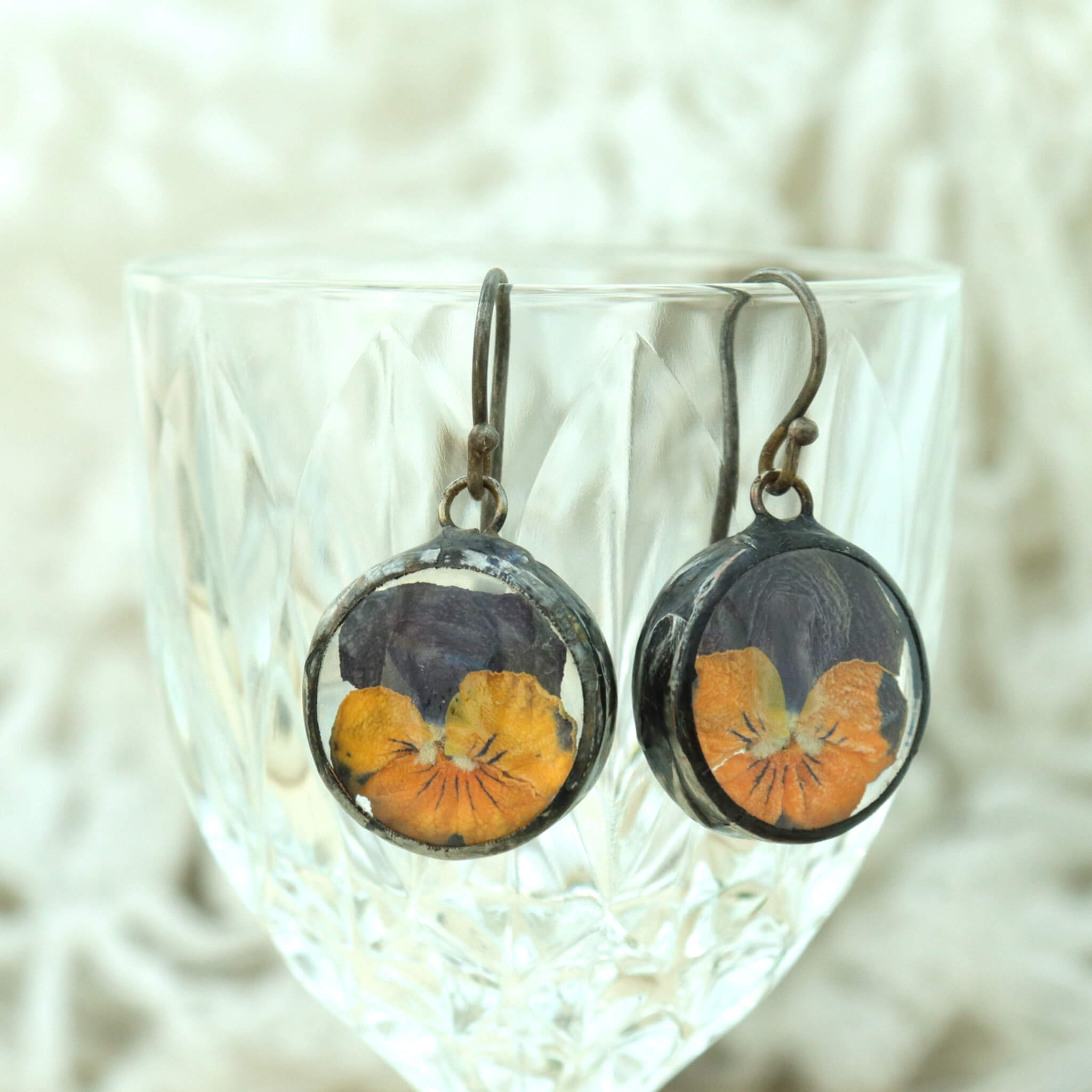 round earrings featuring real pressed pansies hanging from the edge of the glass