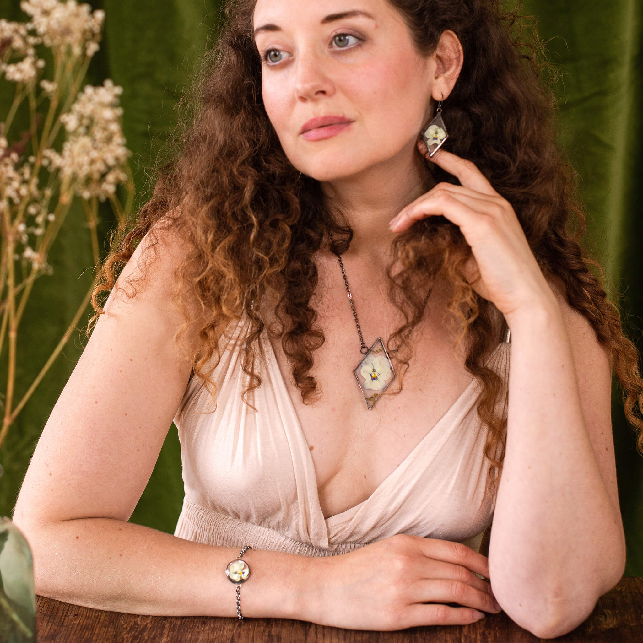 Curly haired woman in ivory dress wearing pansy jewellery