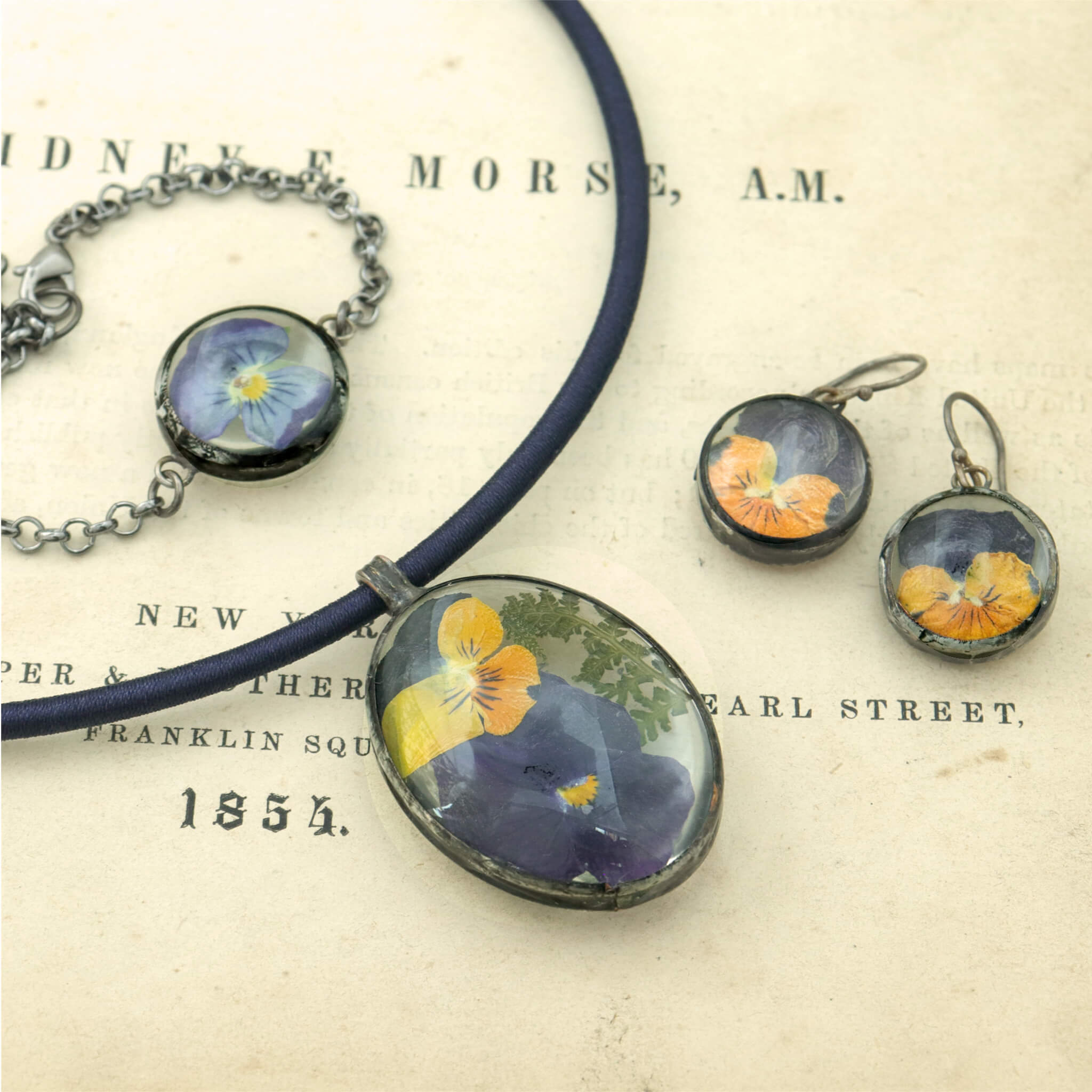 oval necklace and round earrings featuring real pressed pansies lying on an old book