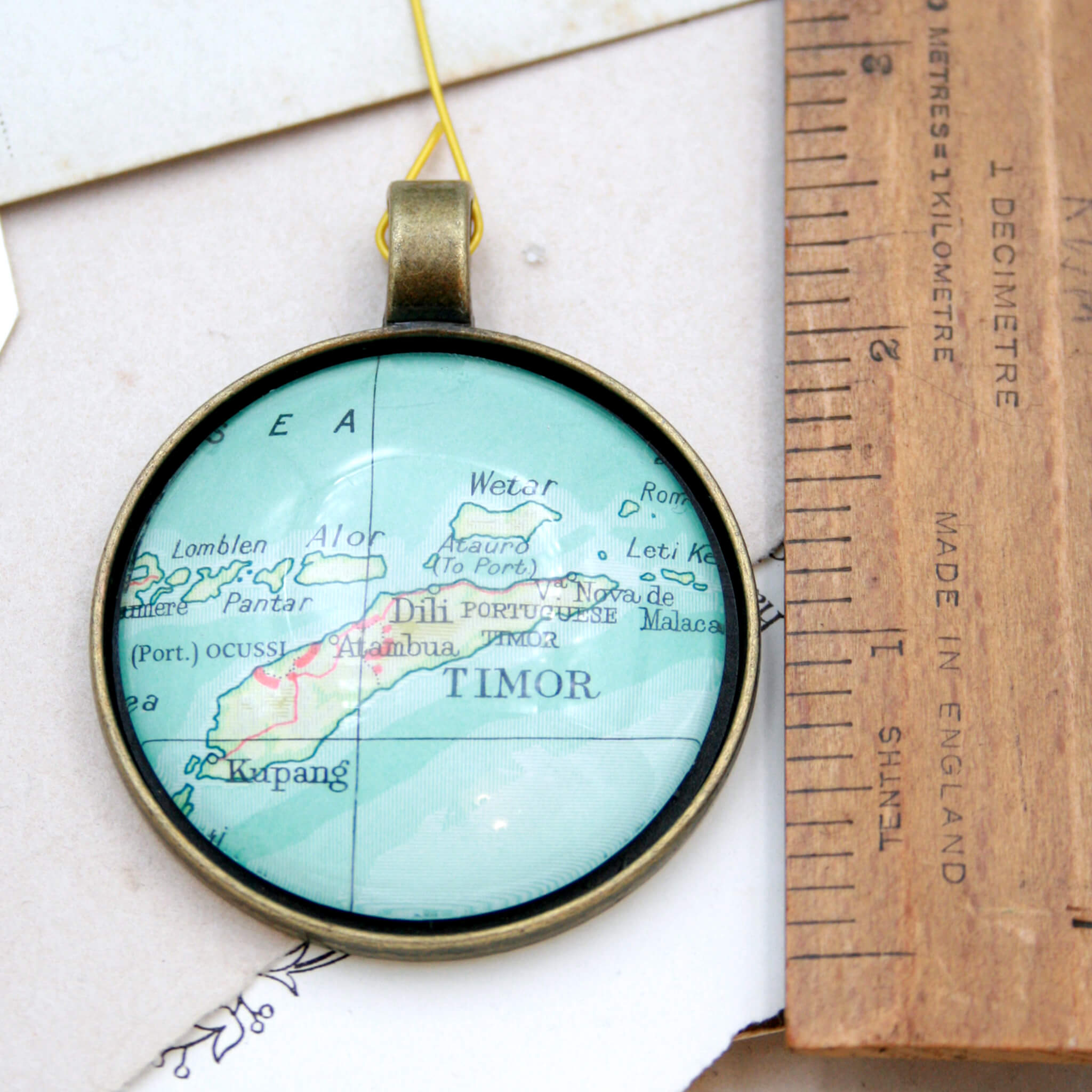 Timor Map Christmas Tree Ornament in bronze tone next to a ruler