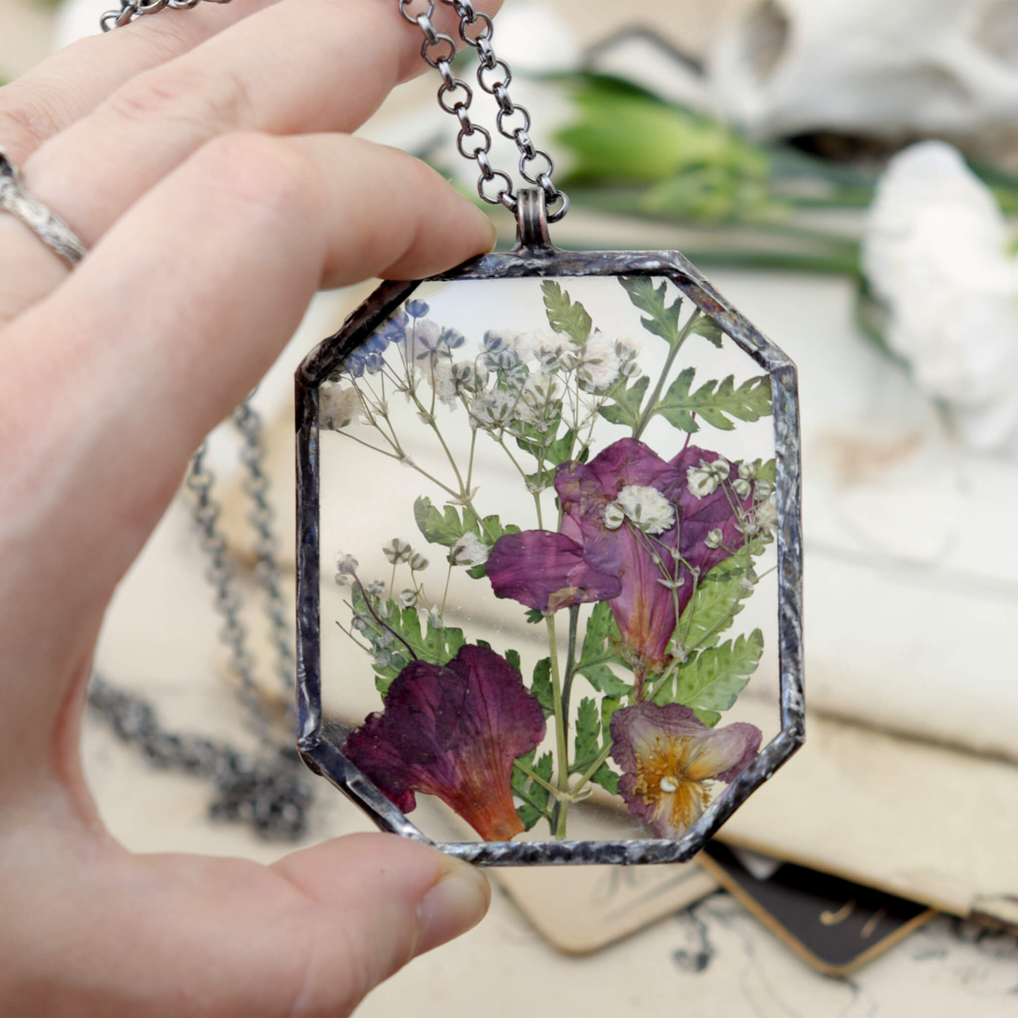Hand holding pink flowers and green ferns in glass and solder necklace 