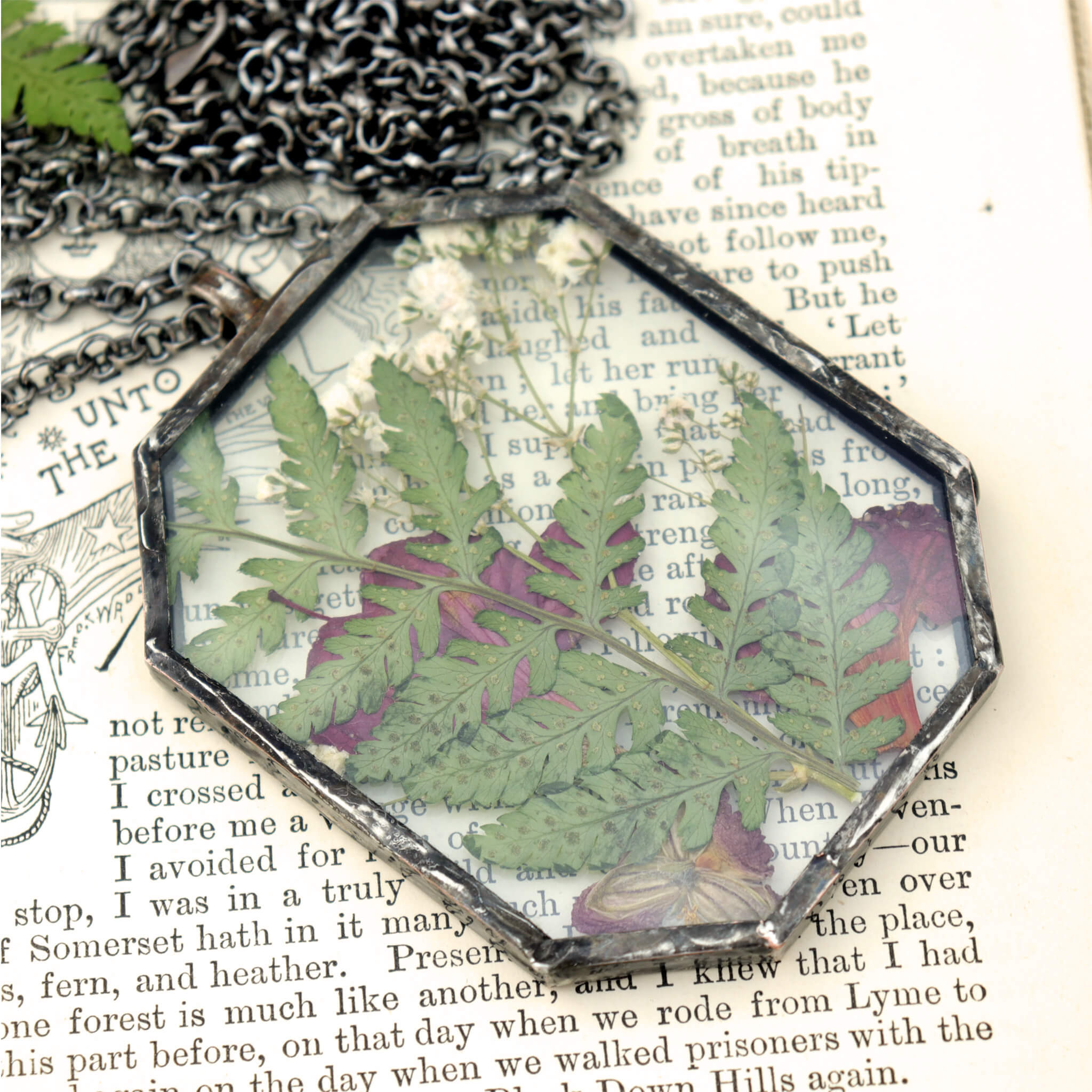 pink flowers and green ferns in glass and solder necklace lying on an old book