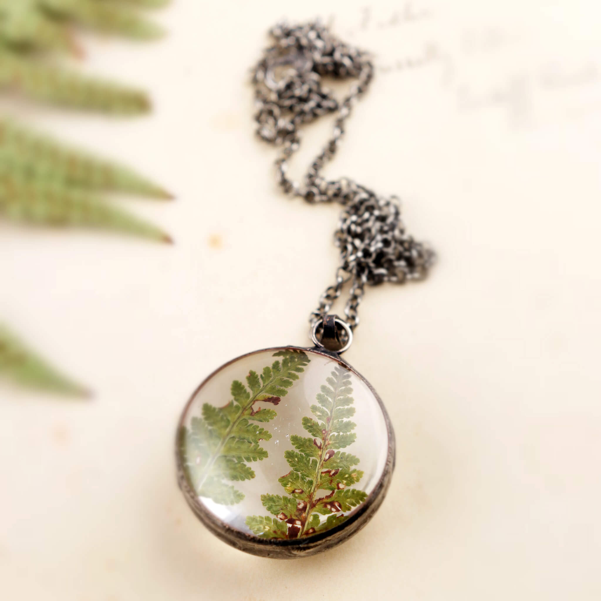 Round necklace with two dry ferns inside the magnifying glass