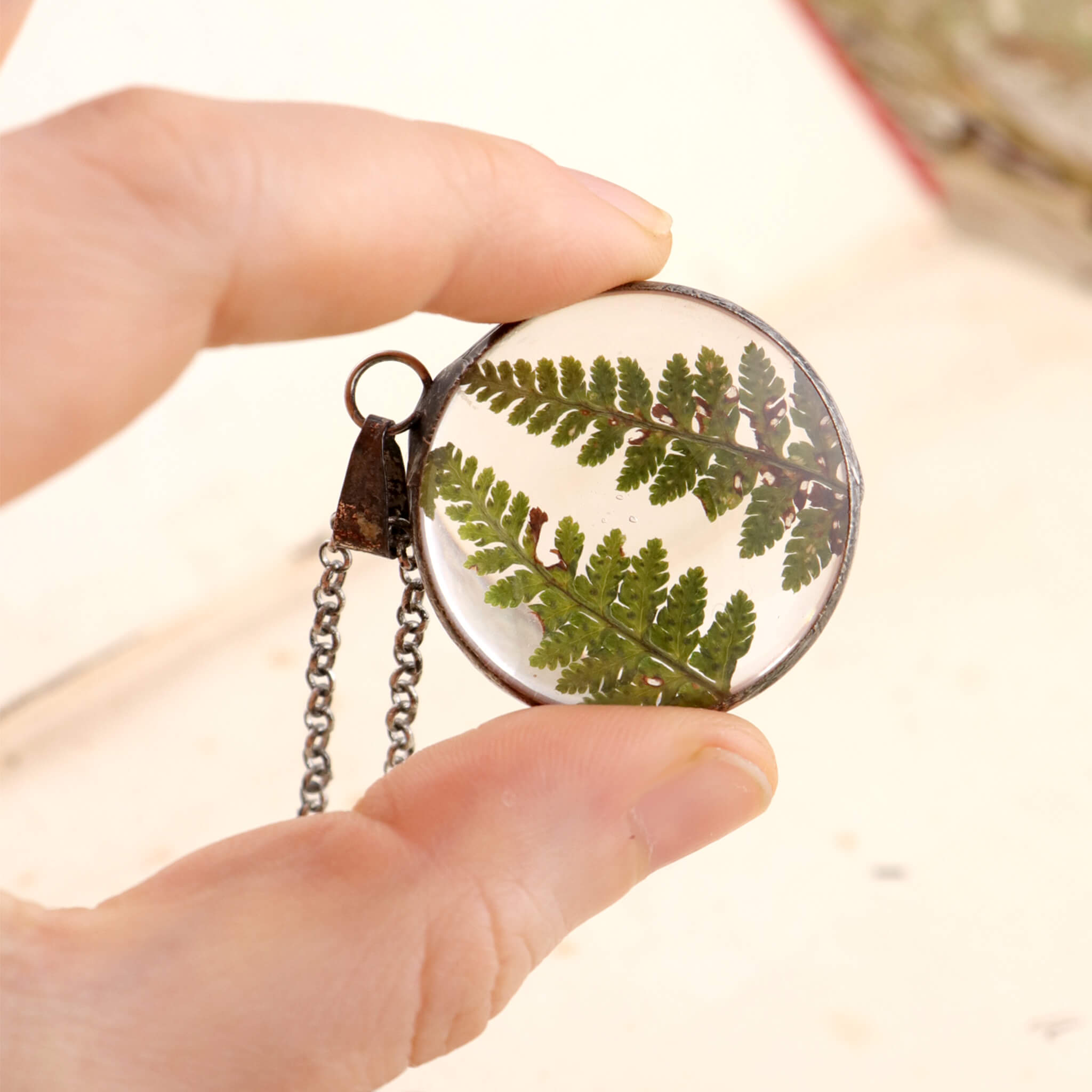 Hand holding Round necklace with two dry ferns