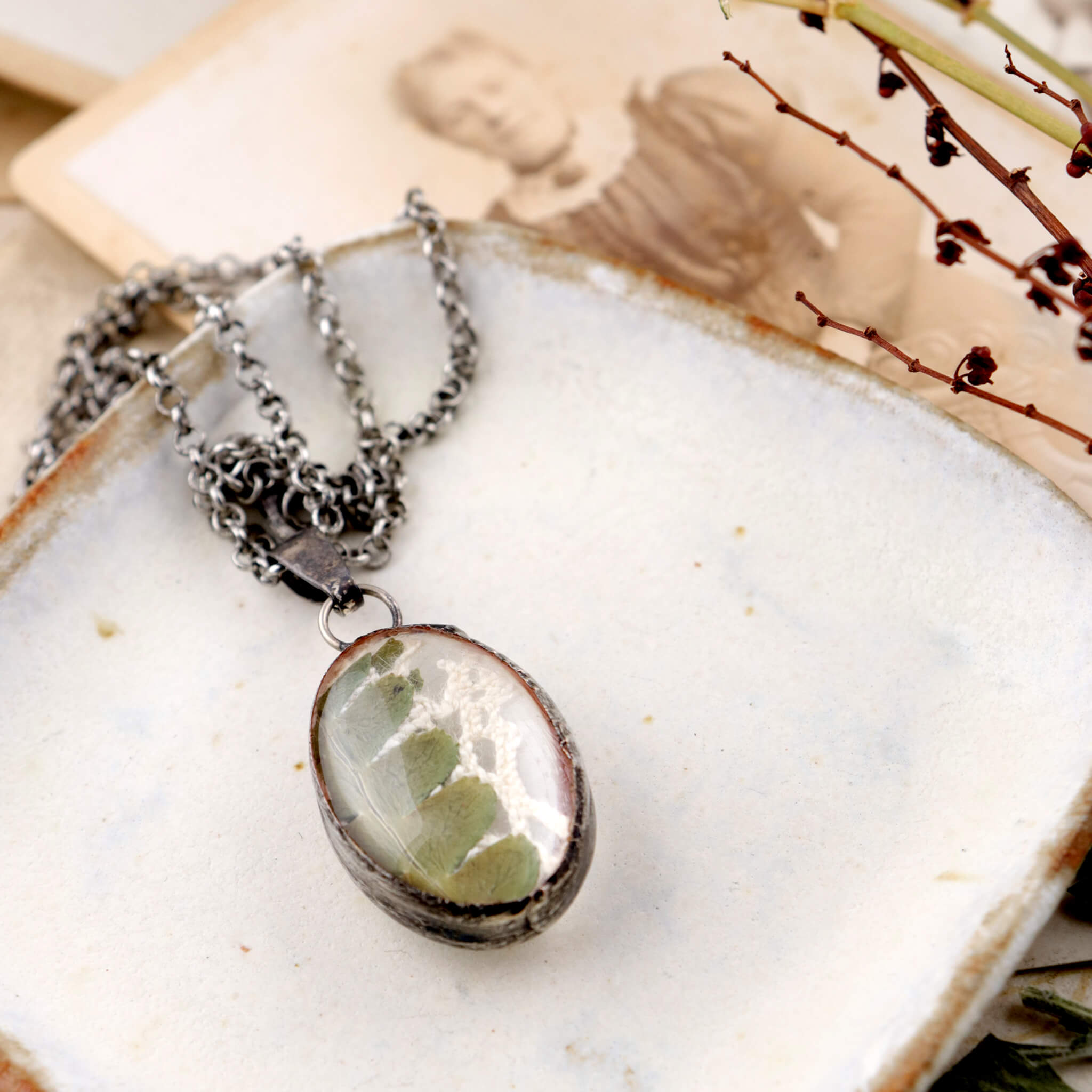 Oval necklace with pressed fern lying on a ceramic plate