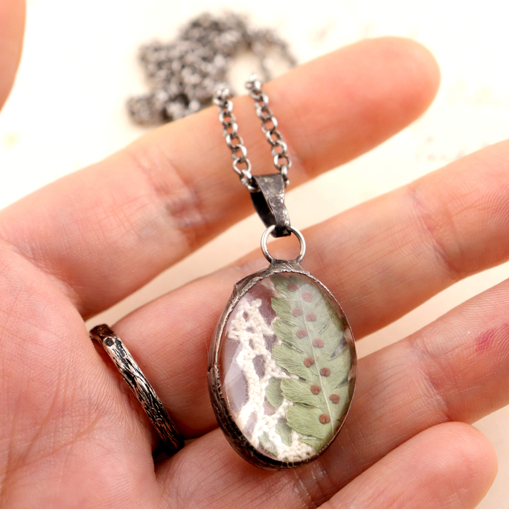 Hand holding oval necklace with real fern