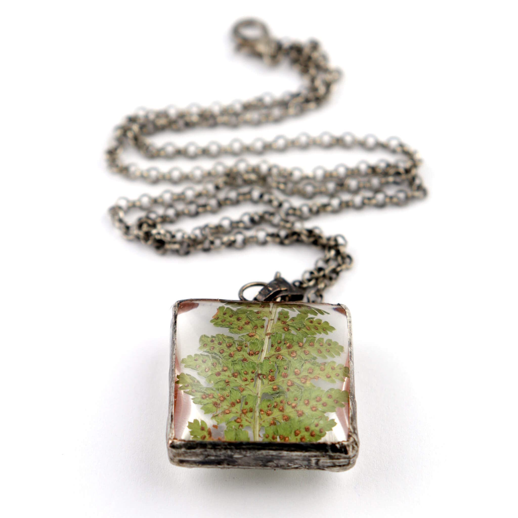 Square necklace with dry fern inside the magnifying glass