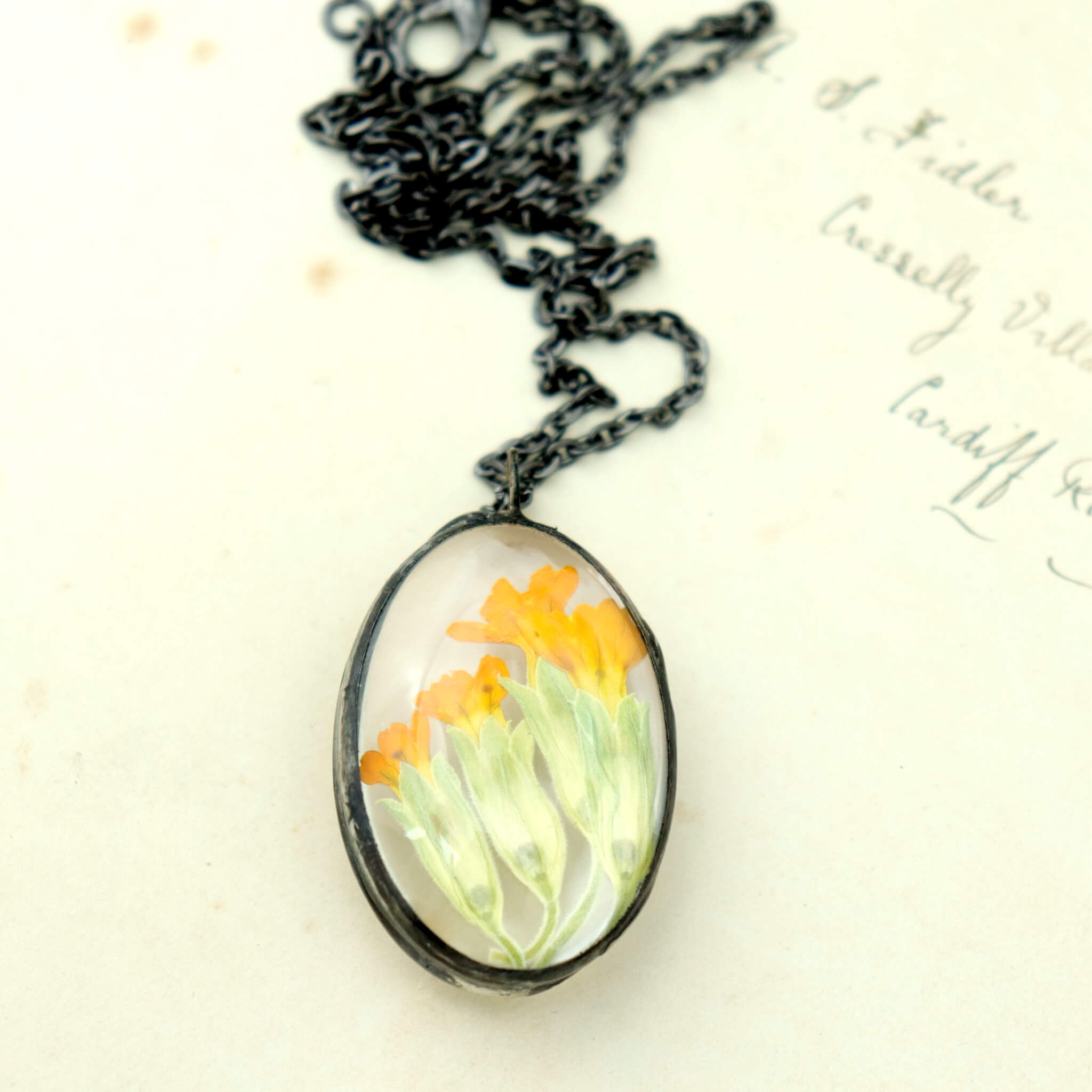 Primroses in soldered glass necklace lying on an old letter