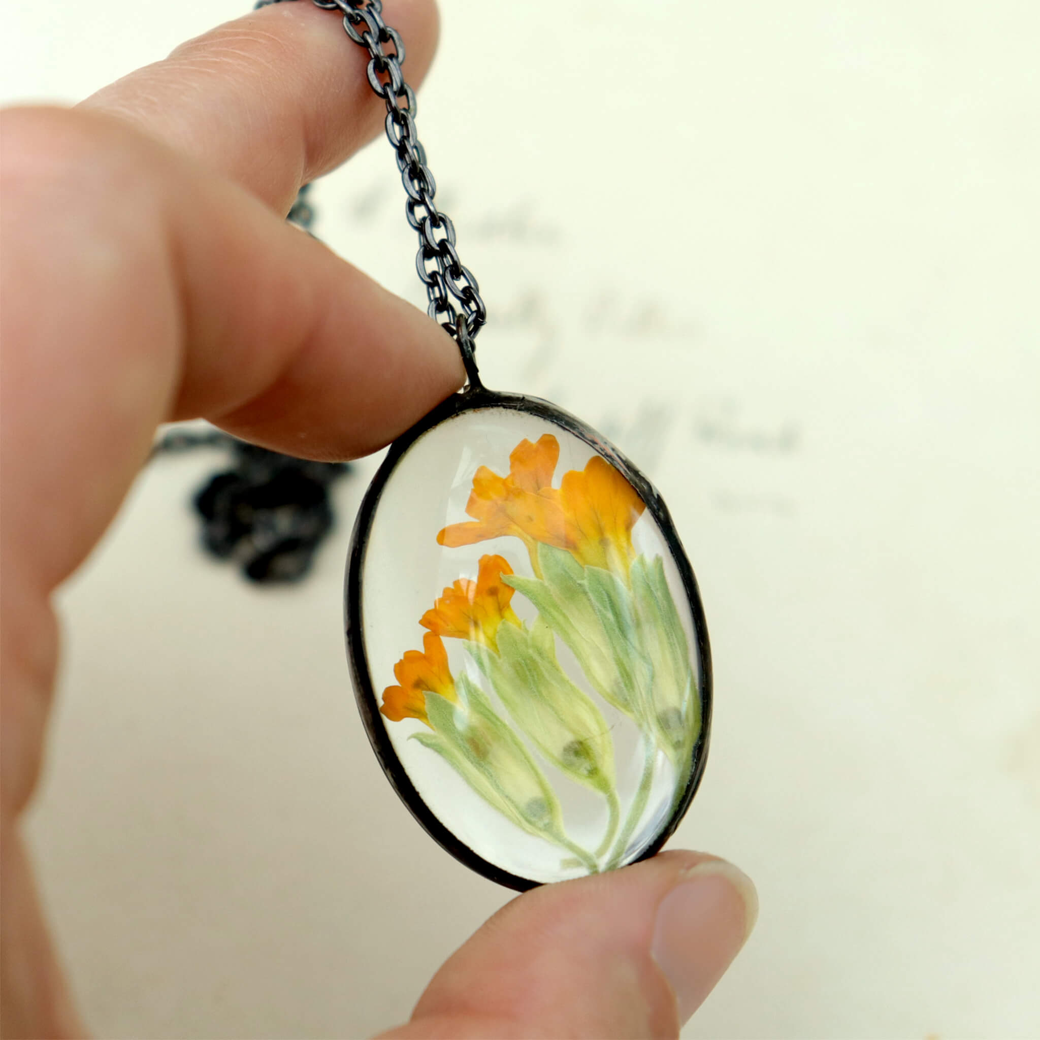 Hand holding soldered glass necklace with primrose flowers