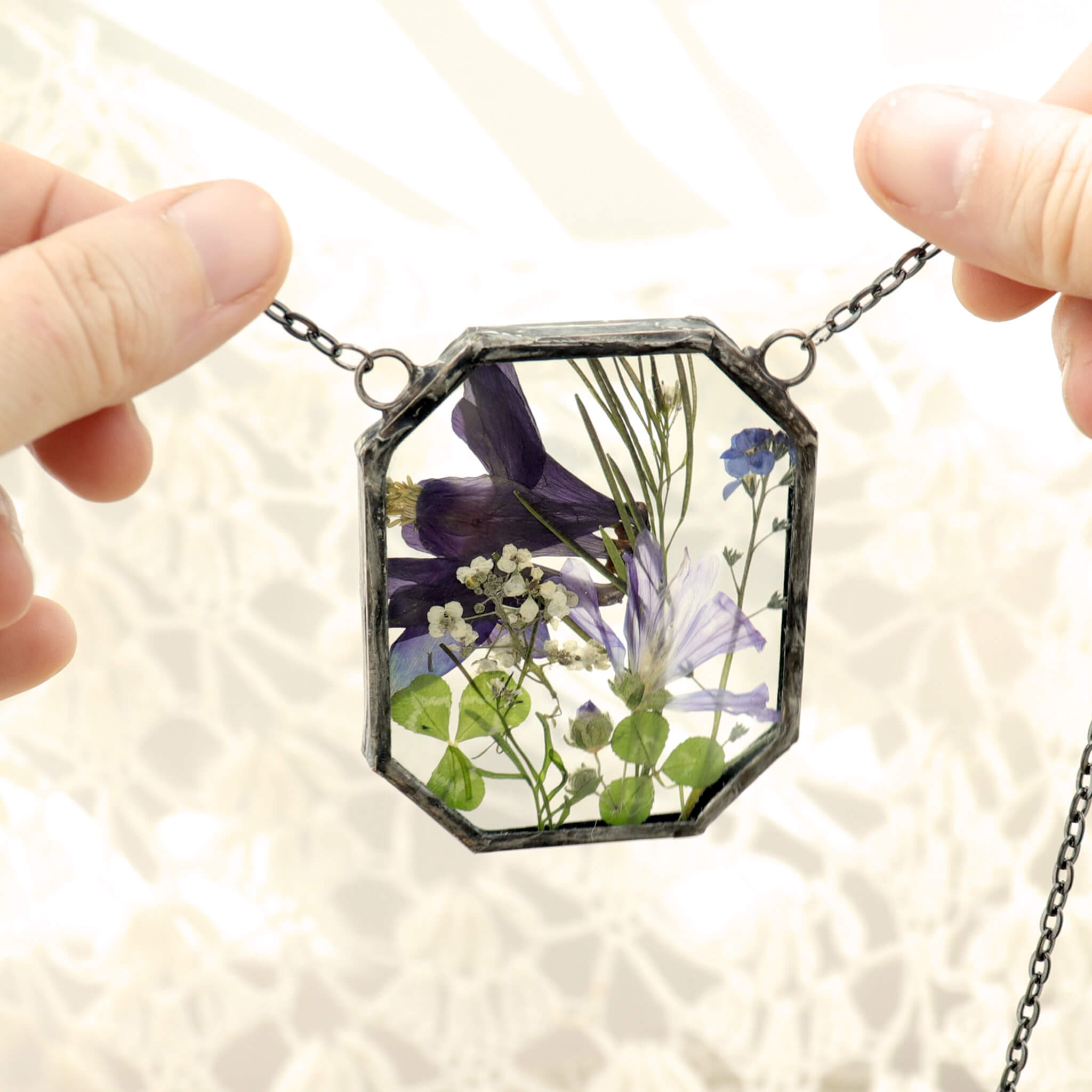 dark indigo flowers and greenery in glass and solder necklace being held in hands