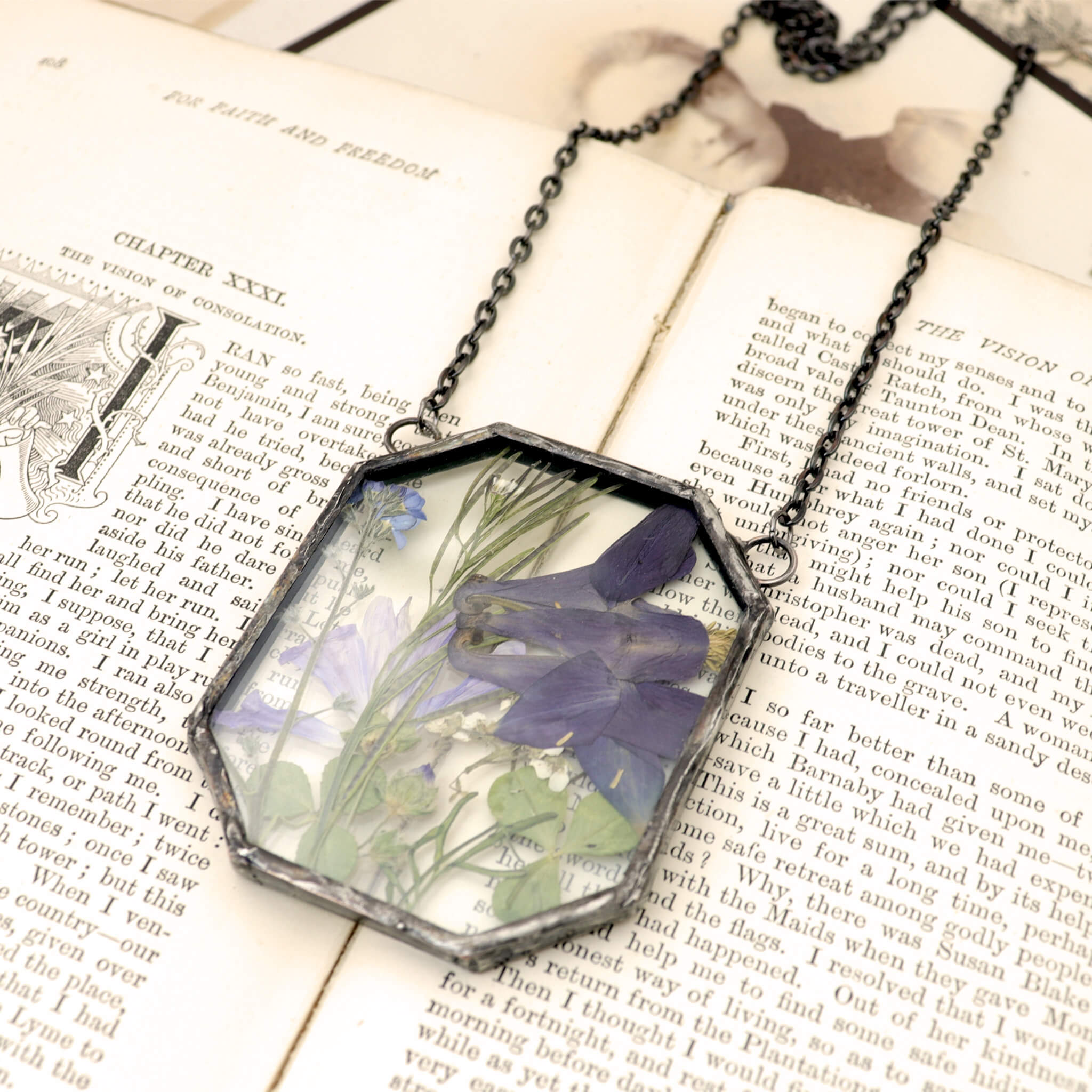 dark indigo flowers and greenery in glass and solder necklace lying on an old book