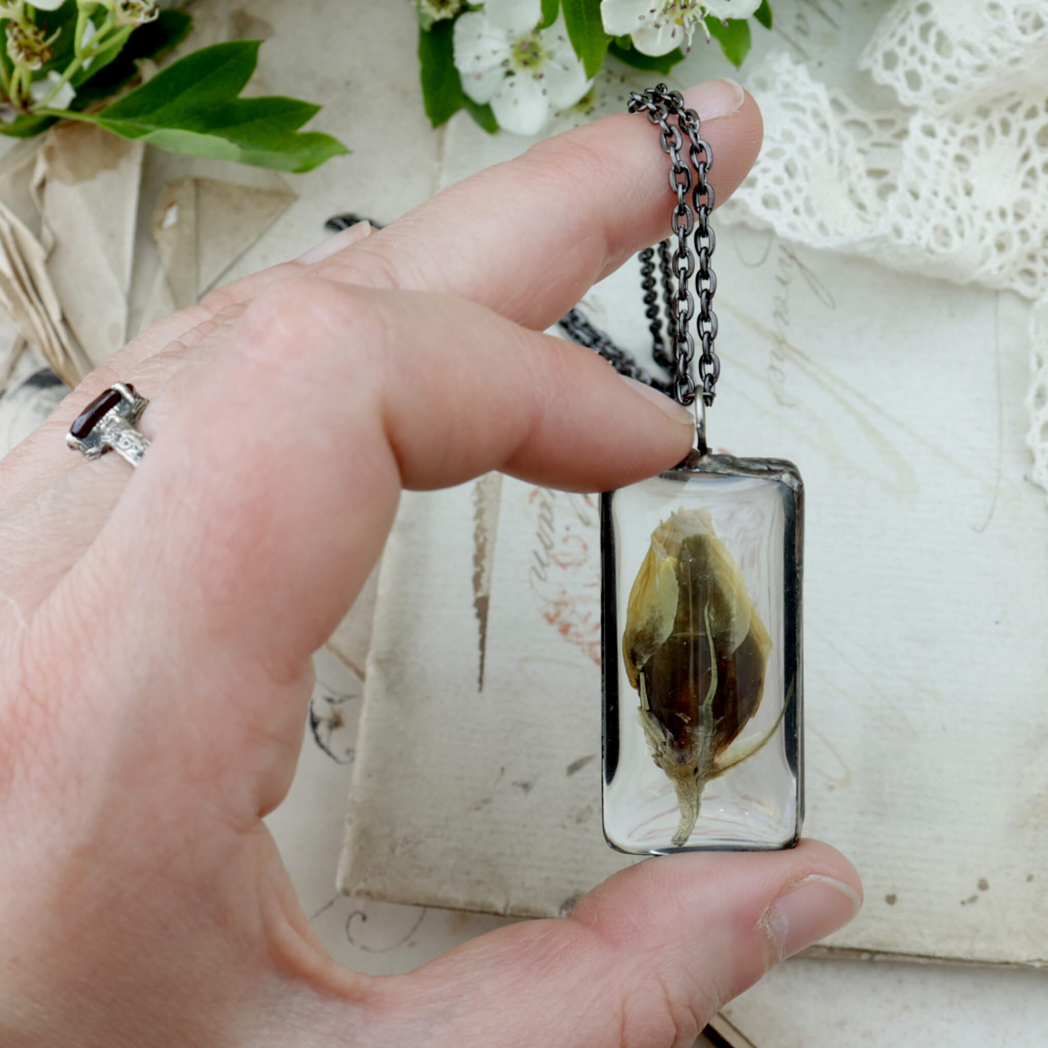 Hand holding a pendant necklace with Eustoma flower bud framed in stained glass