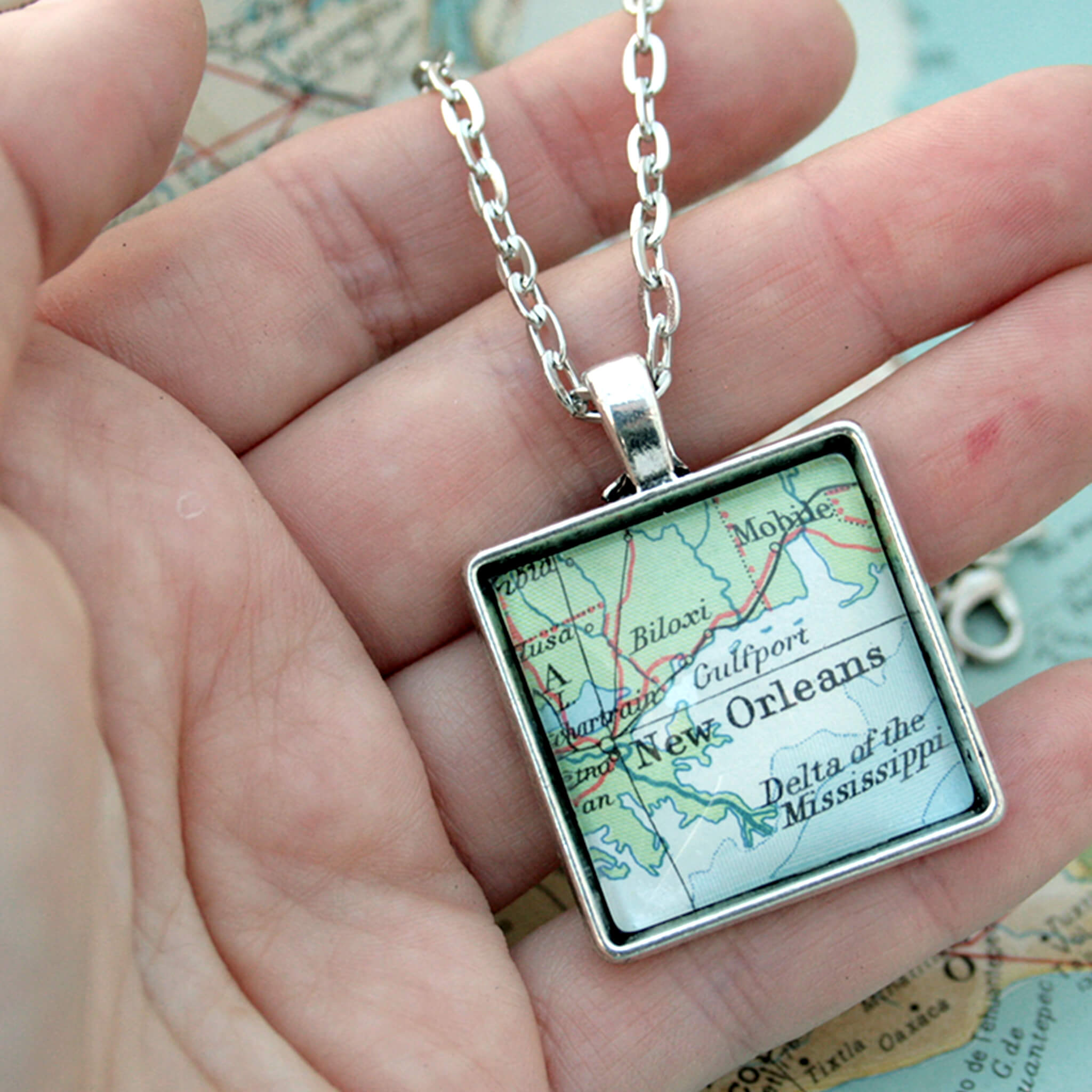 Hand holding silver coloured, square pendant necklace featuring map of New Orleans