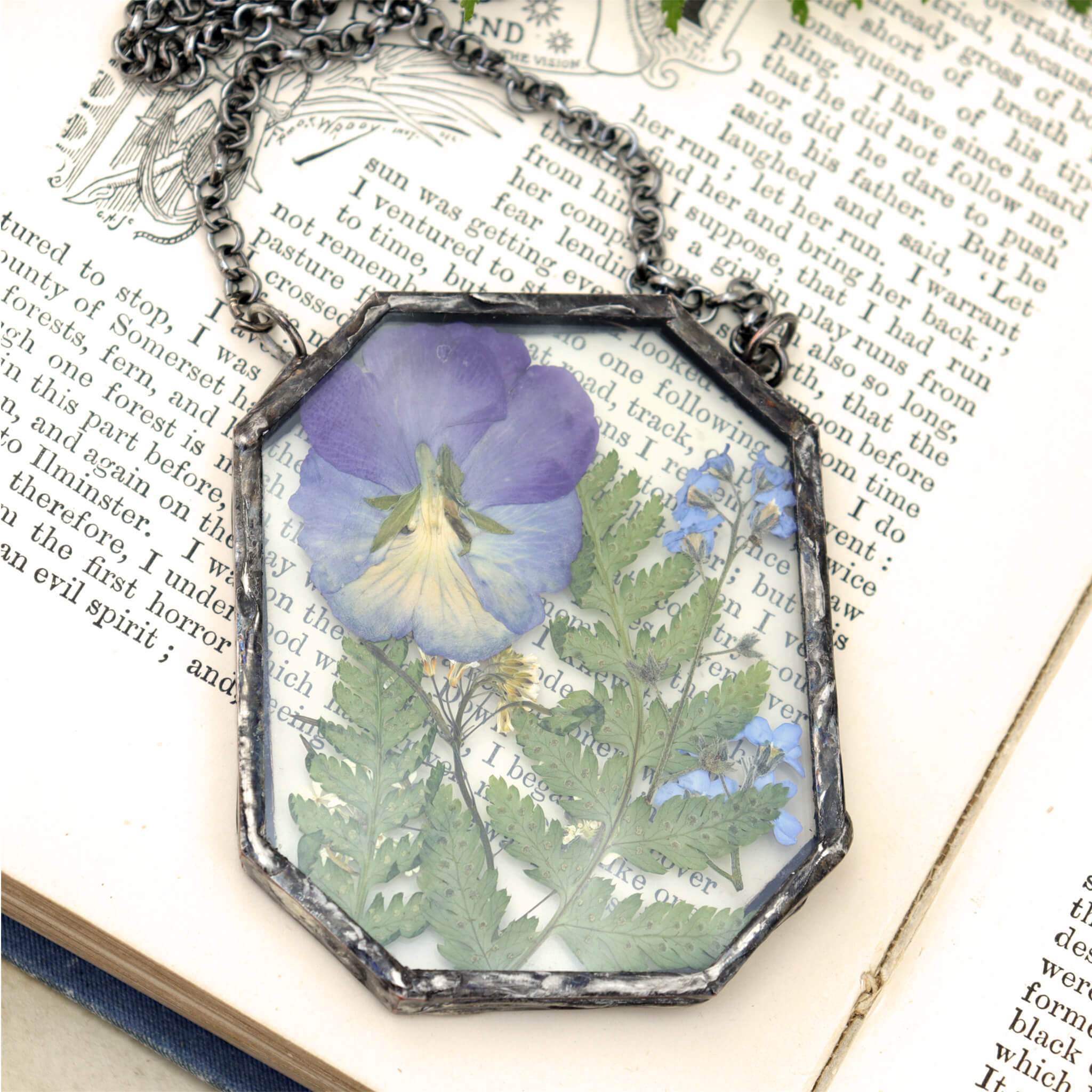 violet flowers and greenery in glass and solder necklace lying on an old book