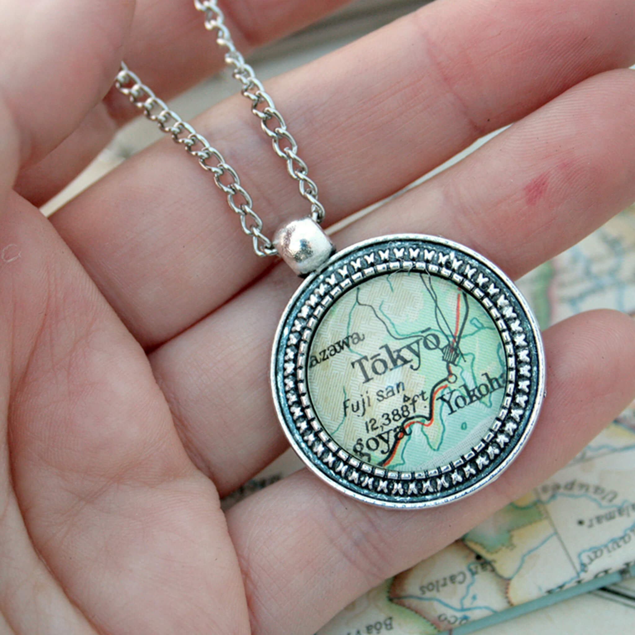 Hand holding Silver coloured pendant necklace with map of Tokyo