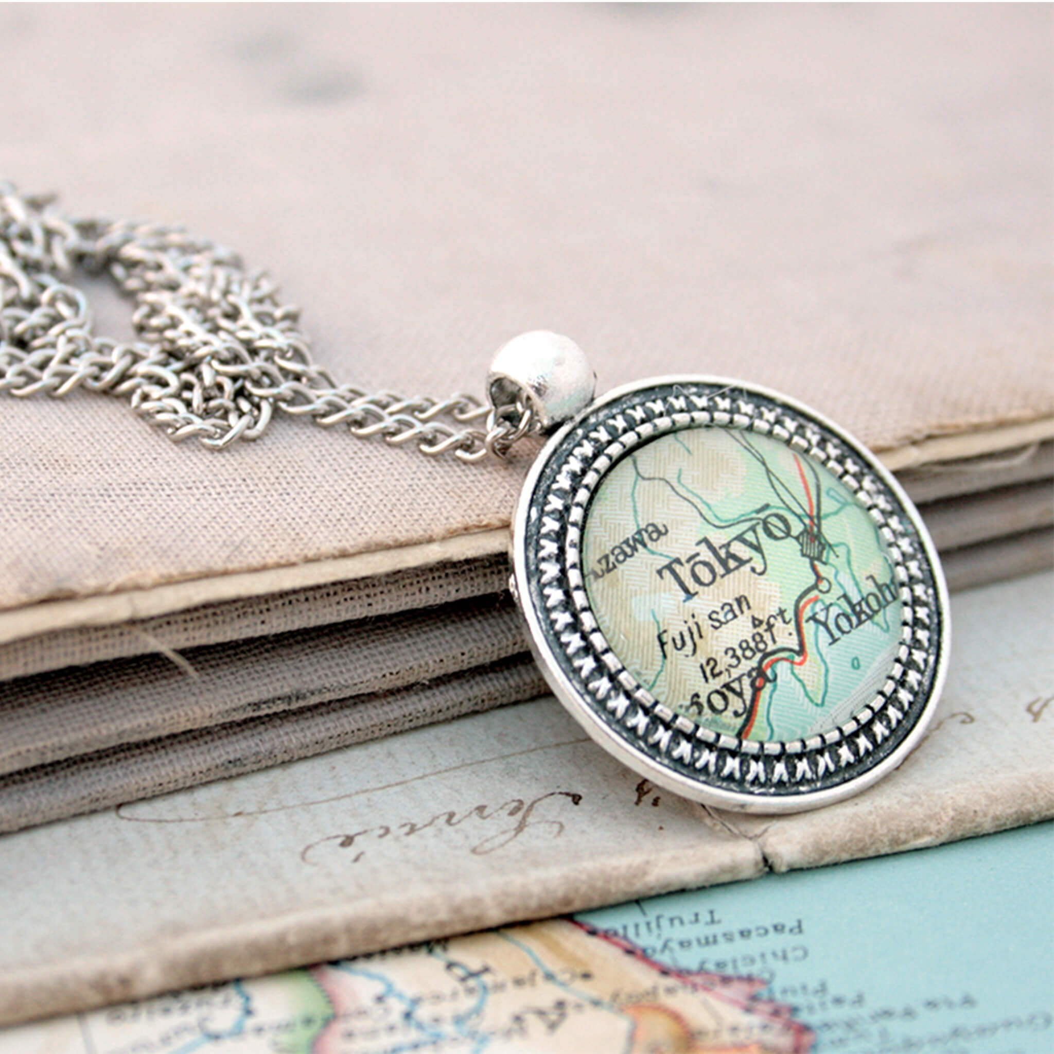 Silver coloured pendant necklace with map of Tokyo leaning on the book