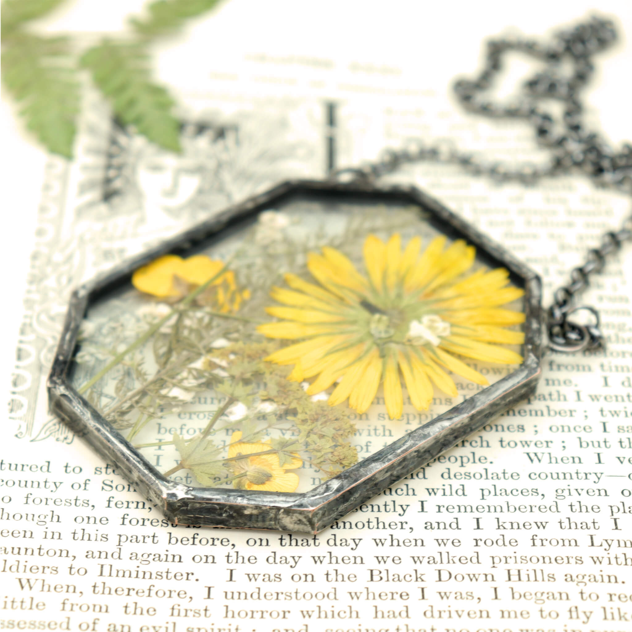 yellow flowers and greenery in glass and solder necklace lying on an old book