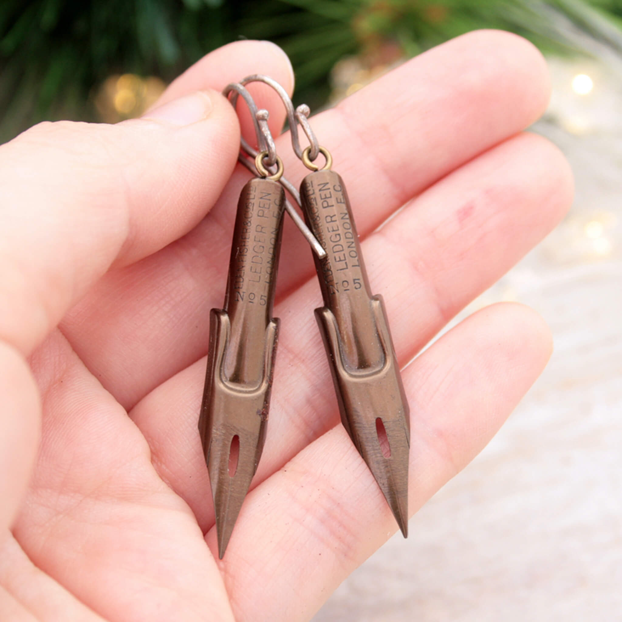 dark academia earrings made of pen nibs in bronze colour being hold in hand