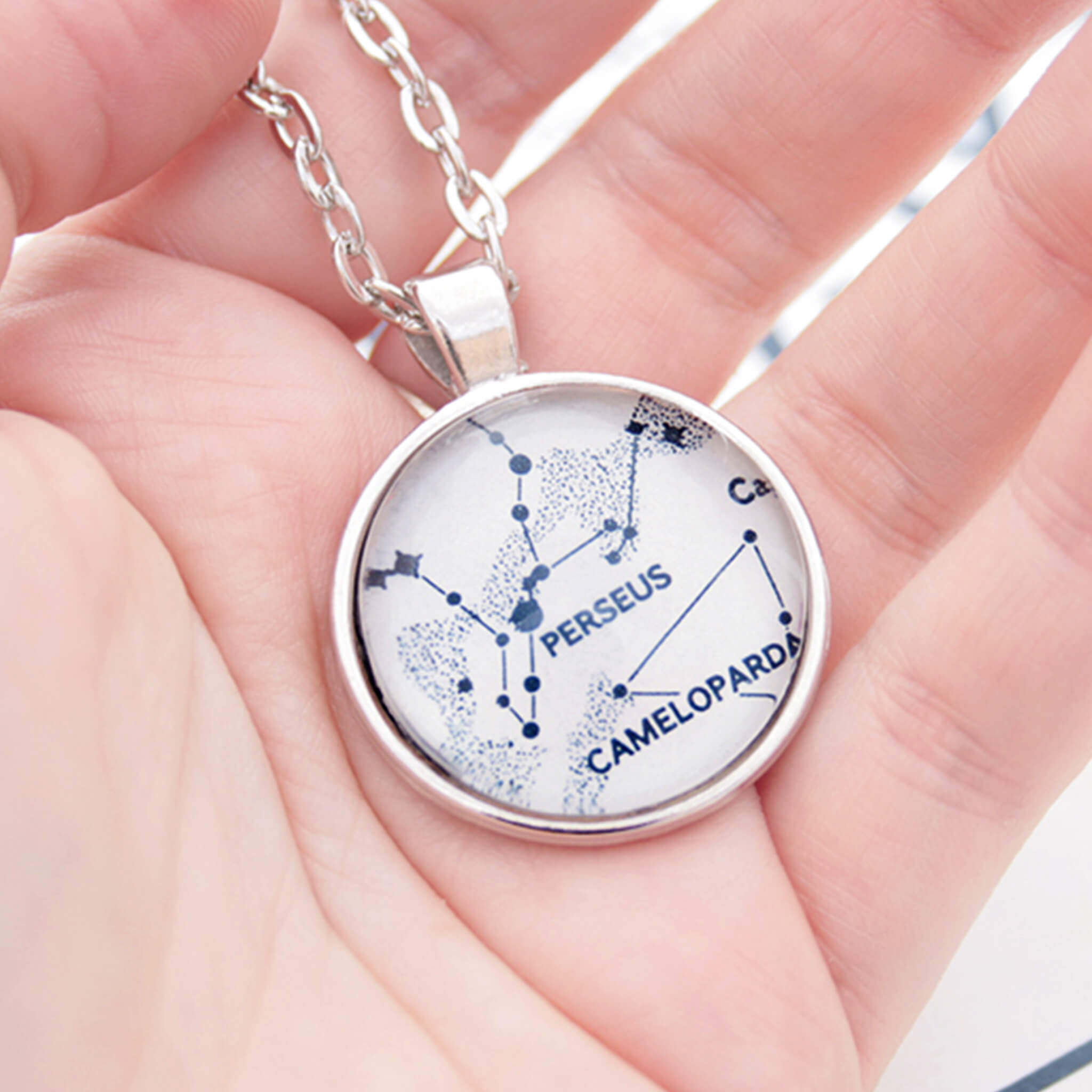 Hand holding silver tone pendant necklace featuring map of Perseus constellations