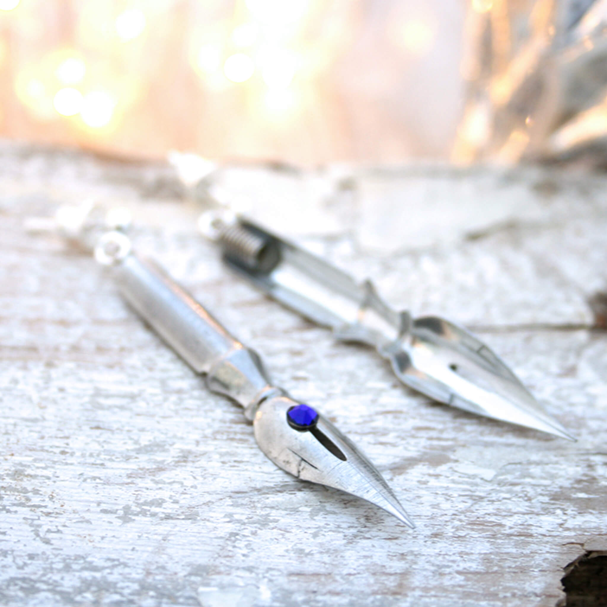 pen nib earrings with cobalt blue crystals on them lying on a white wooden plank